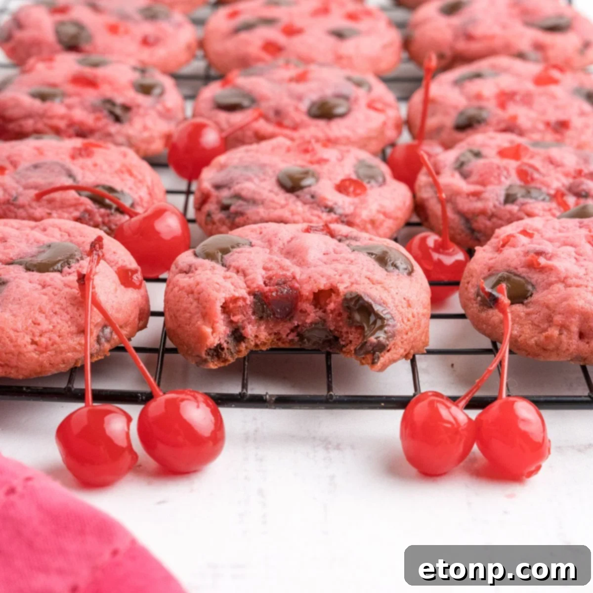 Cherry Chocolate Chip Cookies on a cookie tray with a few cherries on the table in front of the container 
