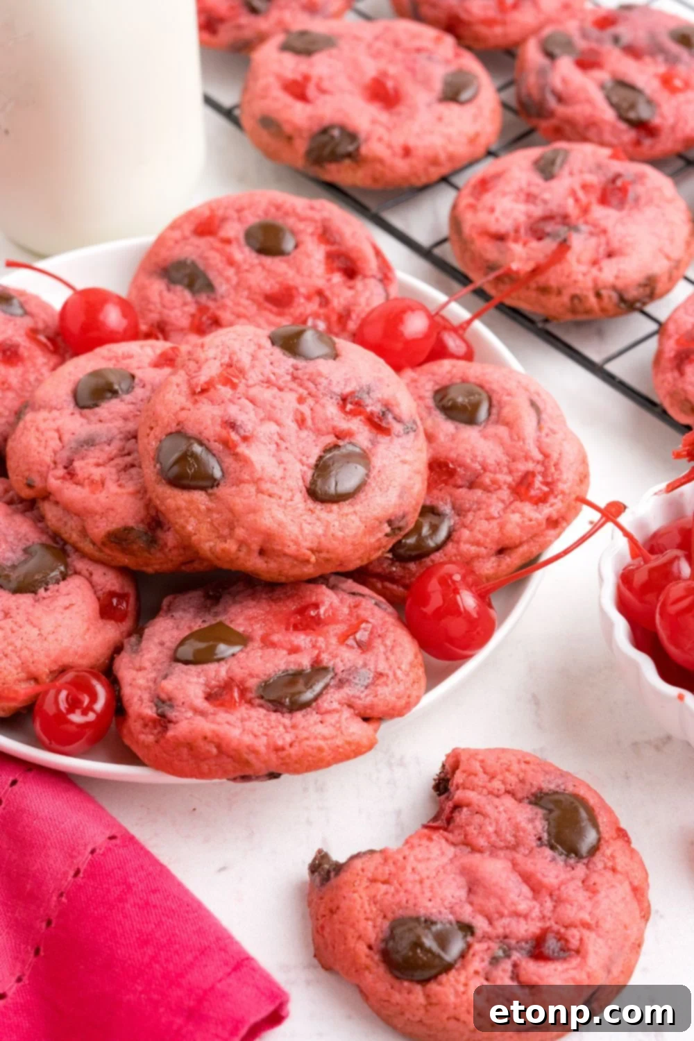 Cherry Chocolate Chip Cookies side view with a plate stacked of cookies and a tall glass of milk beind the plate 