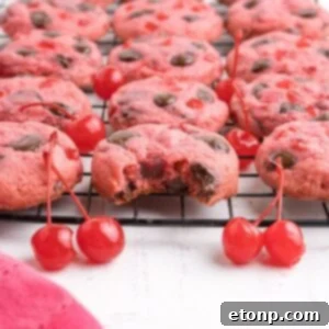 Cherry Chocolate Chip Cookies on a cookie tray with a few cherries on the table in front of the container