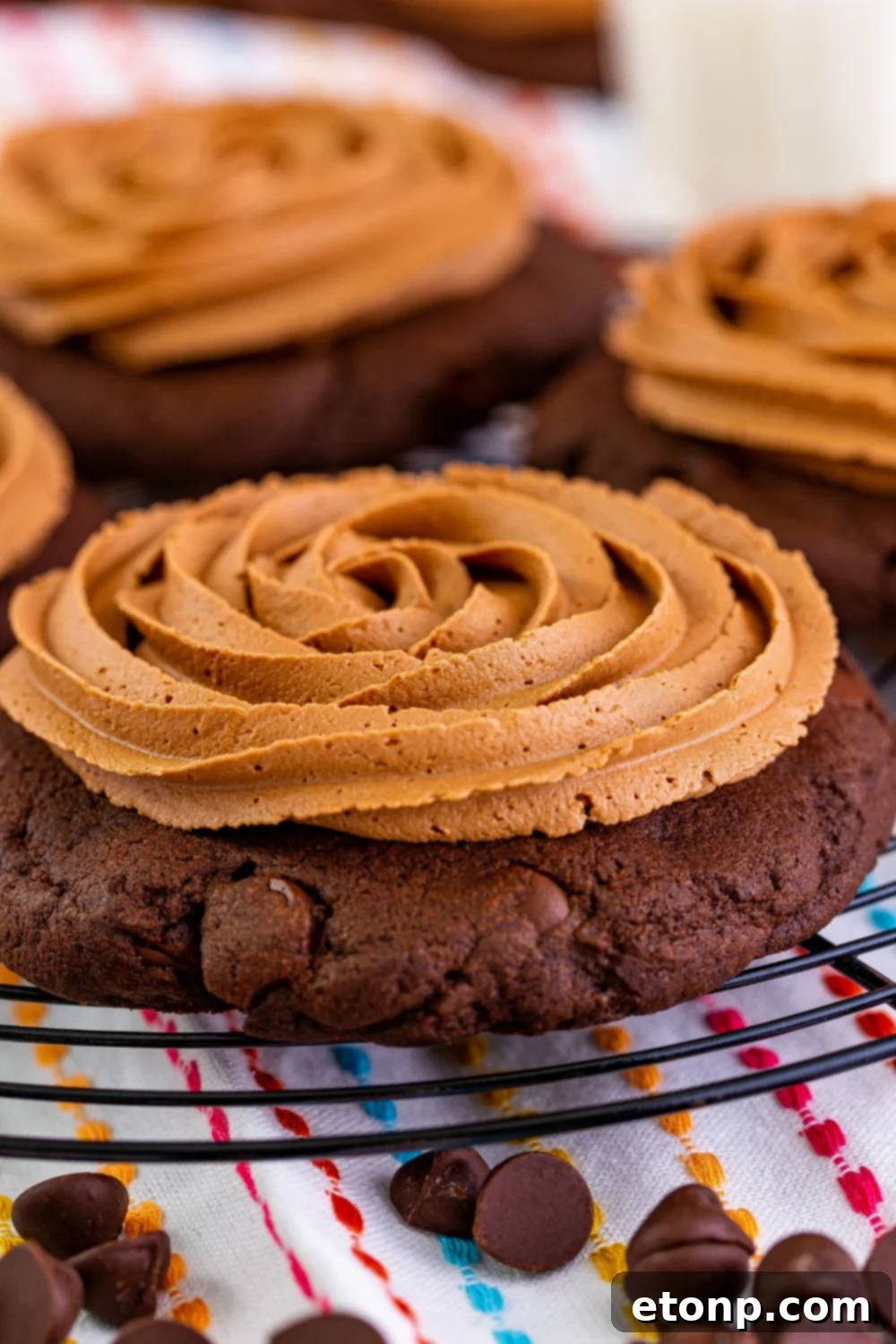 Decadent Chocolate Cake Cookies 22 Close-up of frosted chocolate cake cookies on a metal tray, with a decorative towel and chocolate chips beneath the tray.