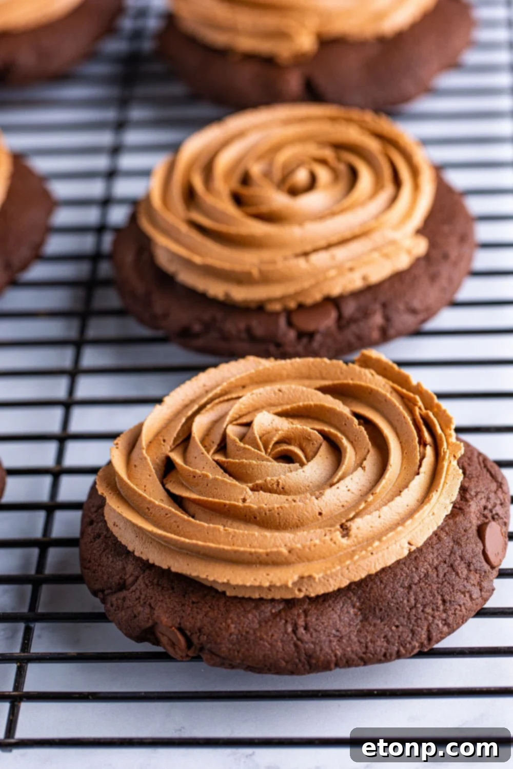 Decadent Chocolate Cake Cookies 5 Freshly baked chocolate cake cookies on a cooling rack, some already adorned with rich chocolate fudge frosting.