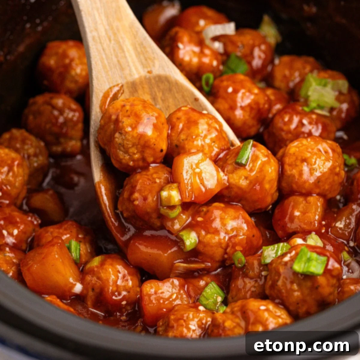 Slow Cooker 3 Ingredient Hawaiian Meatballs in a crockpot with a wooden spoon with some on it 