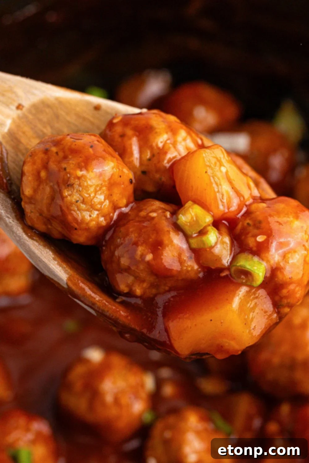 Slow Cooker 3 Ingredient Hawaiian Meatballs on a wooden spoon in a slow cooker 