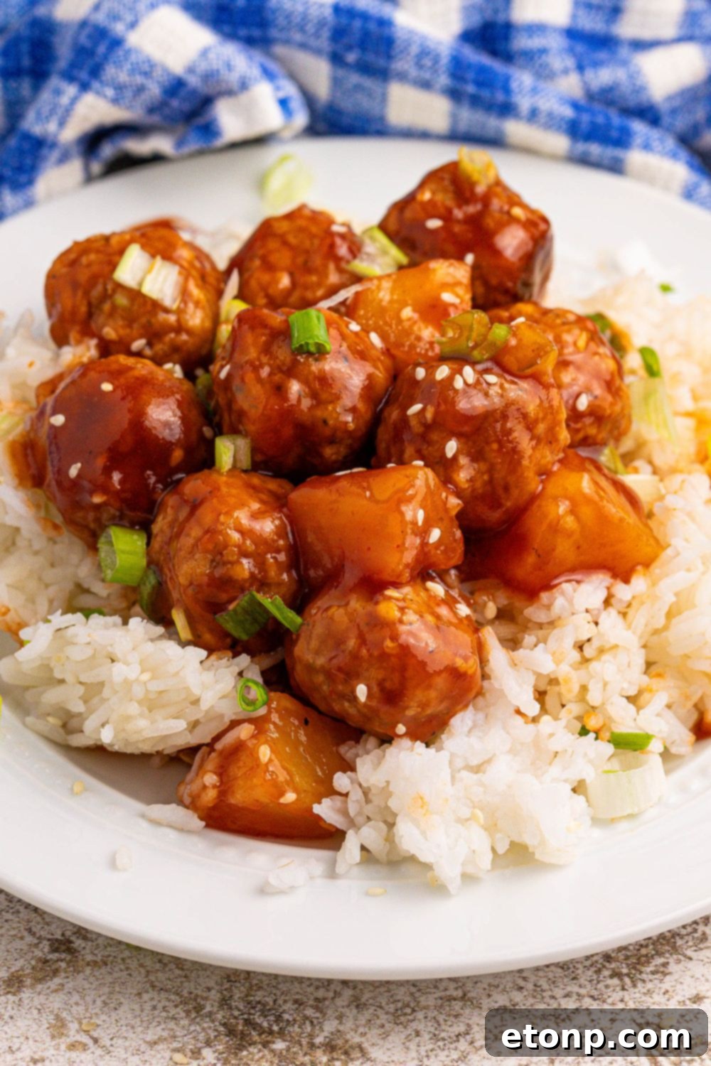 Slow Cooker 3 Ingredient Hawaiian Meatballs on a plate topped iwth sesame seeds and green onions 