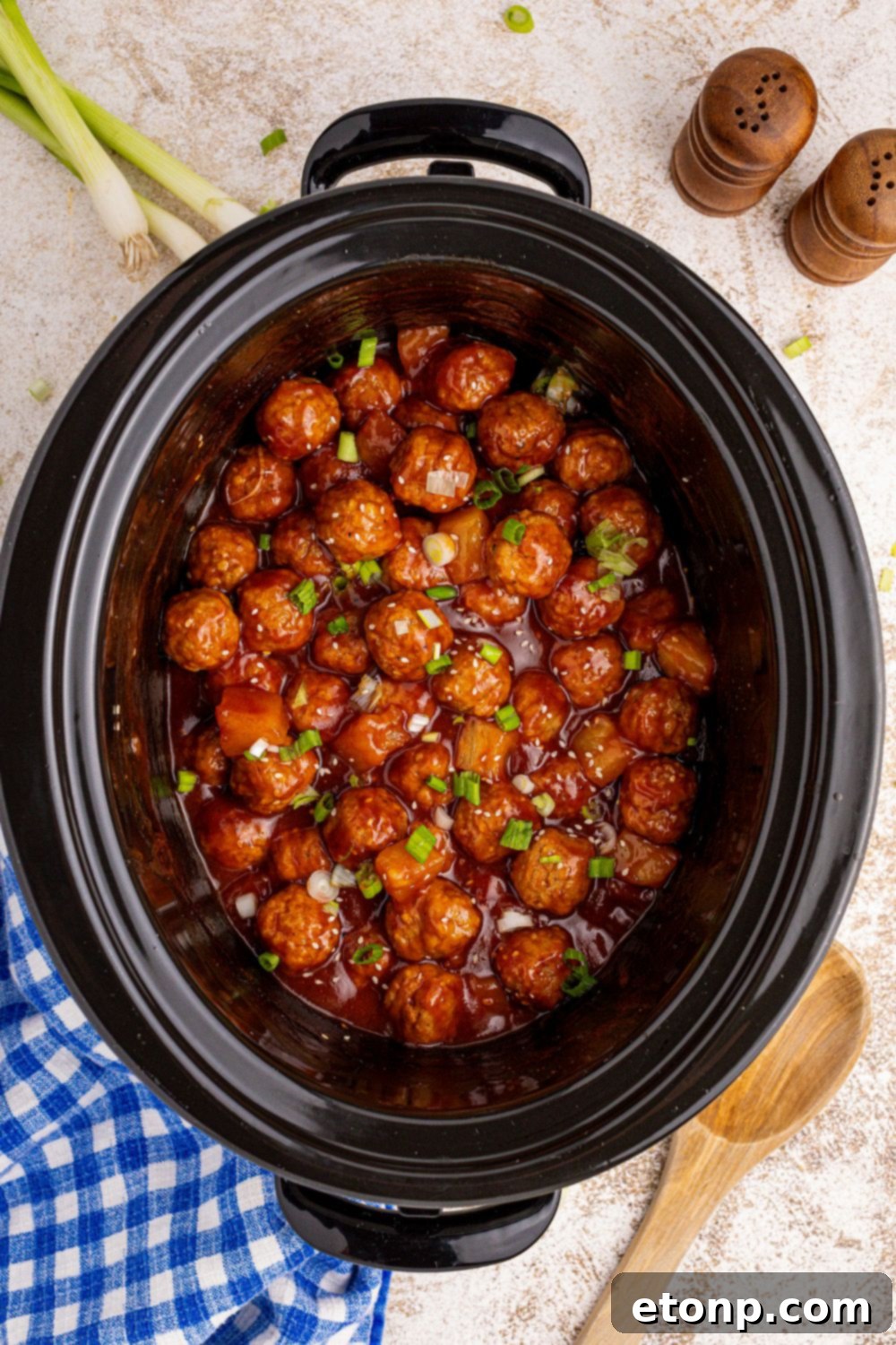 Slow Cooker 3 Ingredient Hawaiian Meatballs in a slow cooker sitting on table with spoon and other items around the slow cooker 