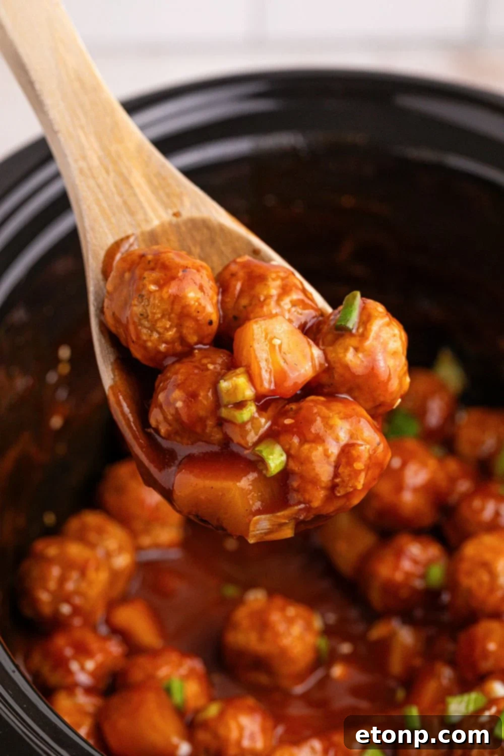 Slow Cooker 3 Ingredient Hawaiian Meatballs in a slow cooker with a spatula with a few meatballs on 