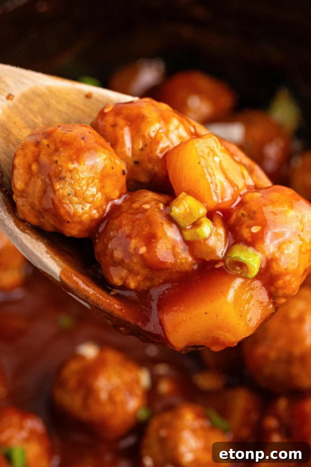 close up of Slow Cooker 3 Ingredient Hawaiian Meatballs on a wooden spoon inside the crockpot 