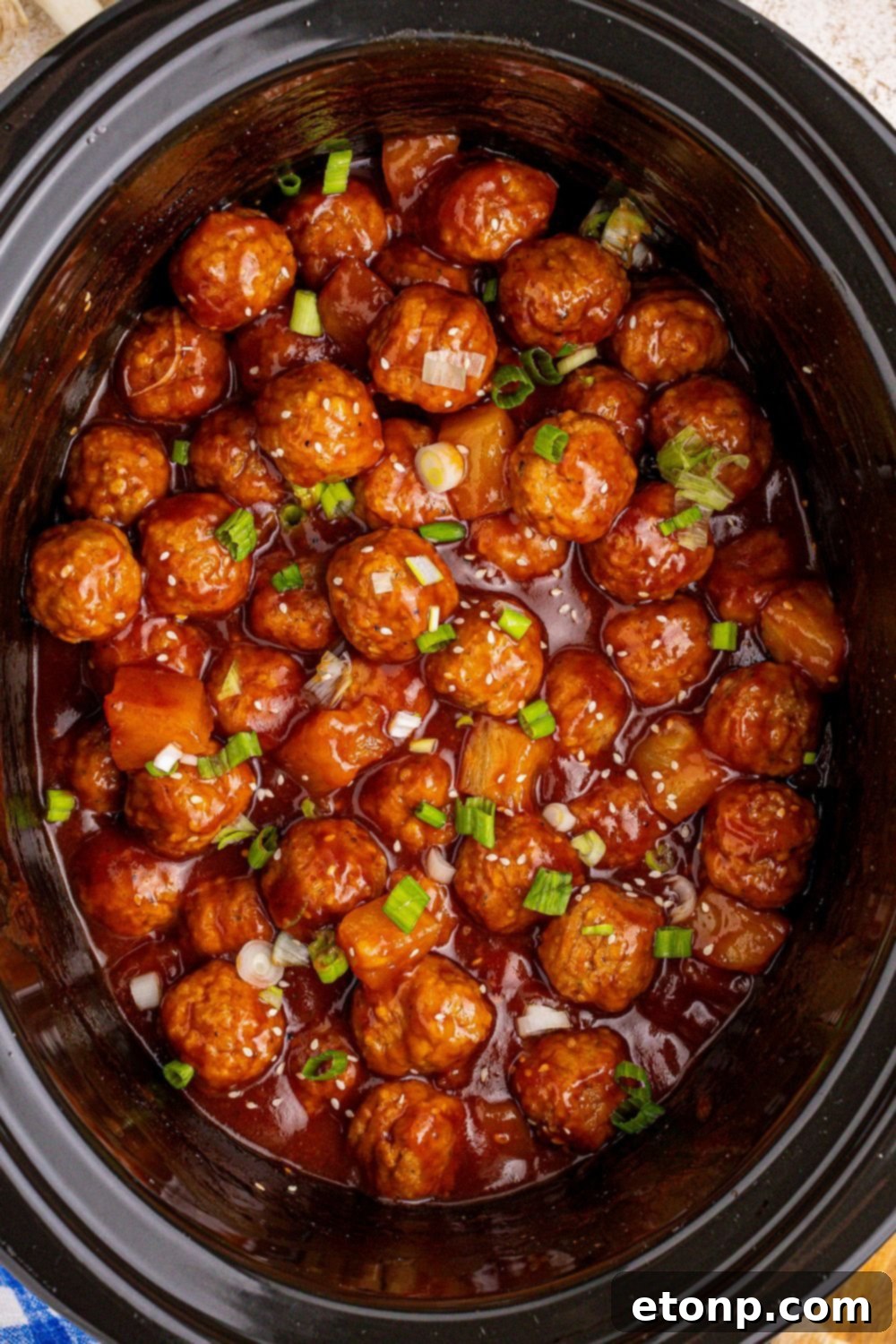 cooked Slow Cooker 3 Ingredient Hawaiian Meatballs with green onions garnished on top of the slow cooker pan