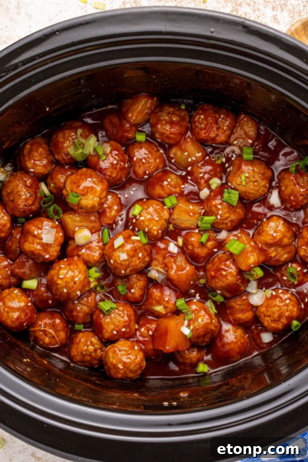 Slow Cooker 3 Ingredient Hawaiian Meatballs in a slow cooker on the table with garnishes on top 