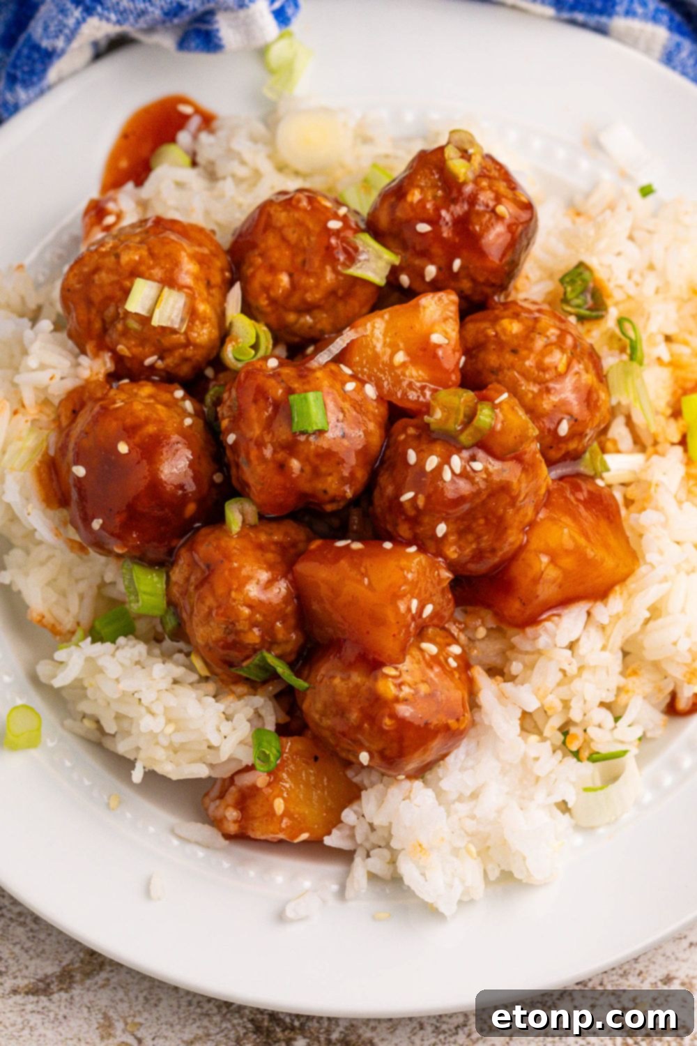 Slow Cooker 3 Ingredient Hawaiian Meatballs on a plate with a bed of rice under it and sesame garnish 