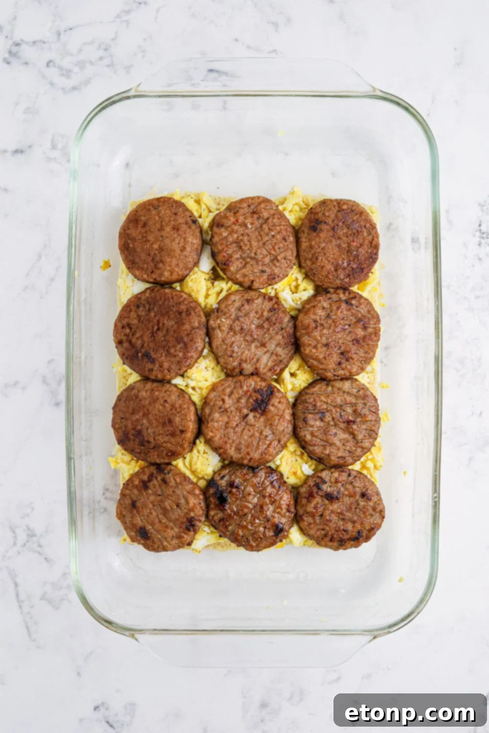 Breakfast Sliders being prepared with eggs and sausage patties on top of the bottom buns 
