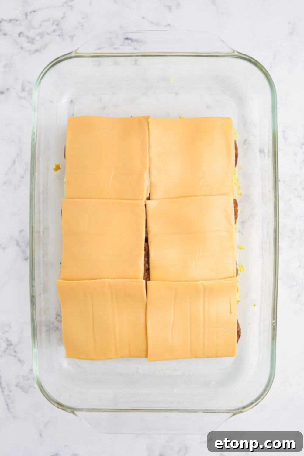Breakfast Sliders being prepared with cheese on top of sasuasge patties in a 9x13 pan 