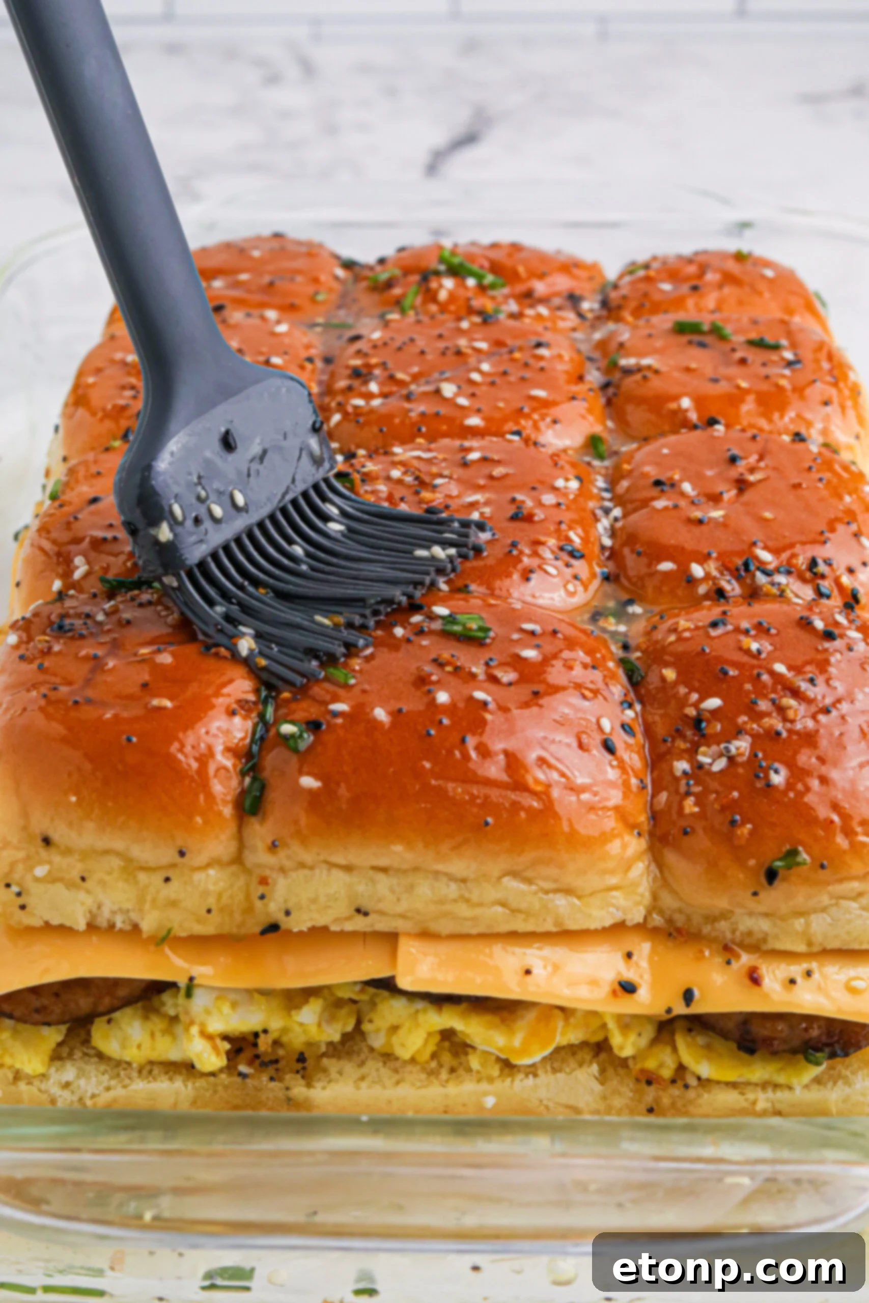 Breakfast Sliders uncut in a baking dish with batter being brushed on top