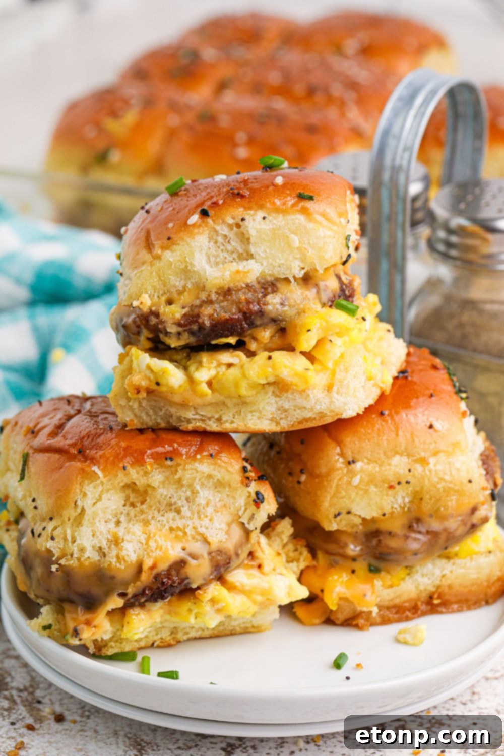 Breakfast Sliders stacked on a plate with a pan of sliders behind it on table 