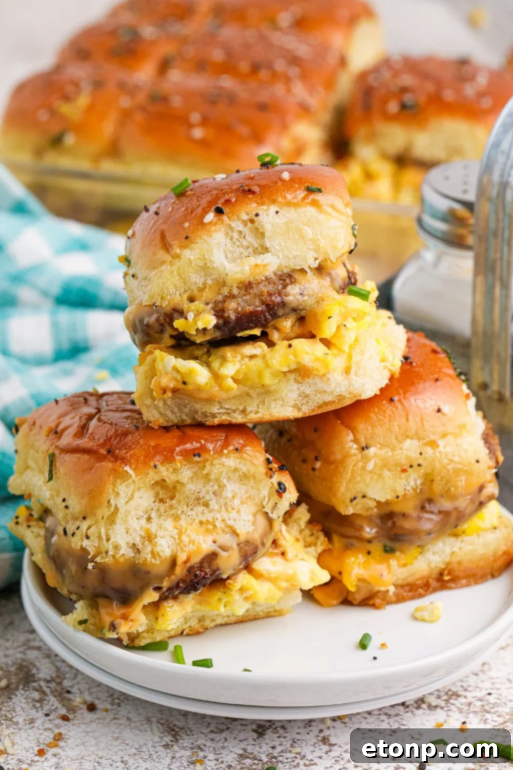 Breakfast Sliders stacked on a plate with a pan of the rest of sliders in the background 