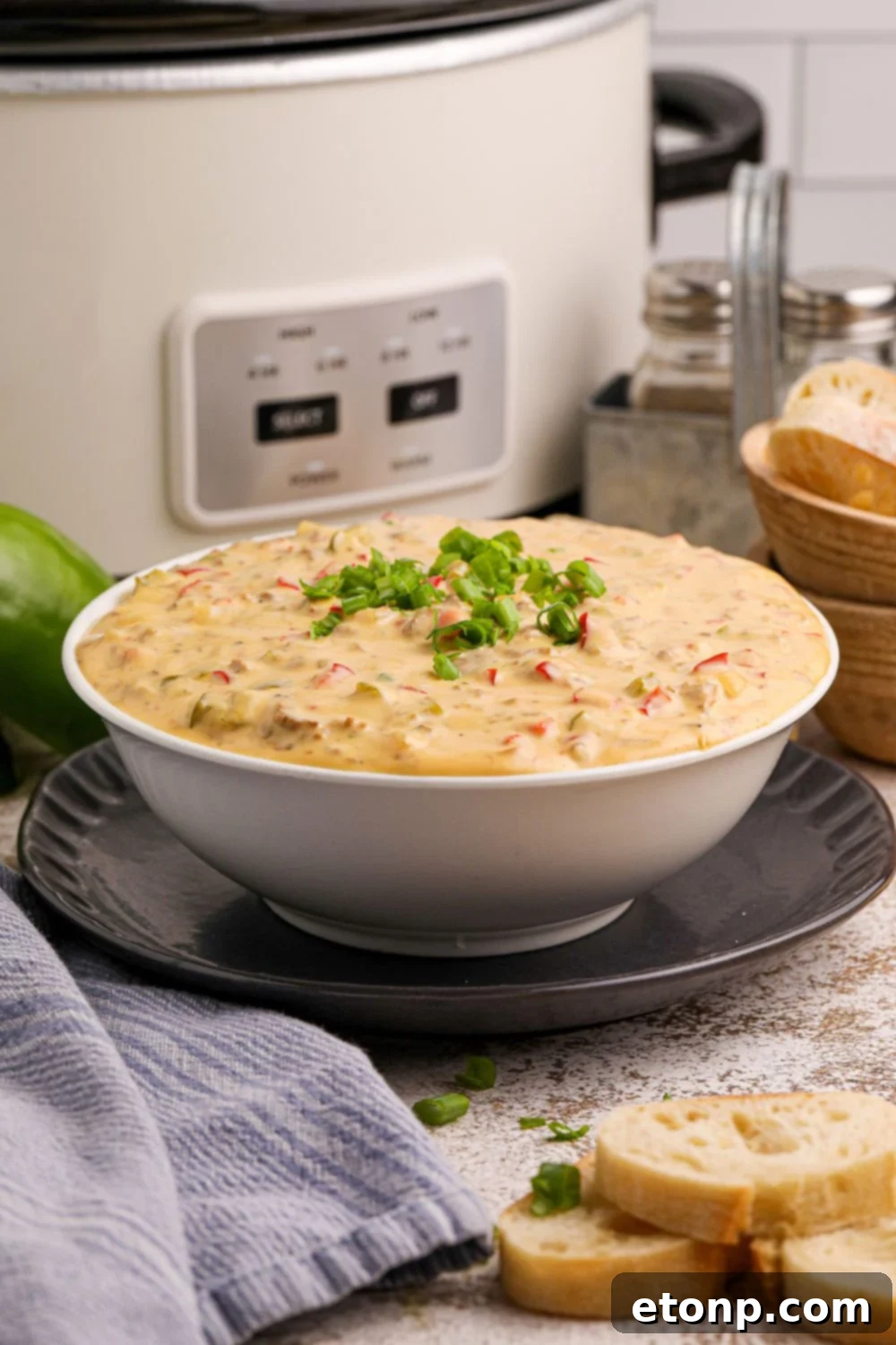 Crock Pot Philly Cheesesteak Dip in a bowl sitting on plate with a slow cooker in the background of the image 