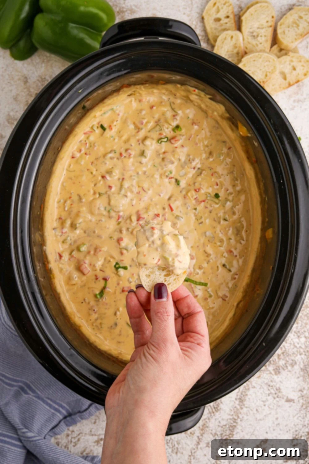 Crock Pot Philly Cheesesteak Dip with a hand and a piece of bread dipped in the creamy dip above the crockpot 