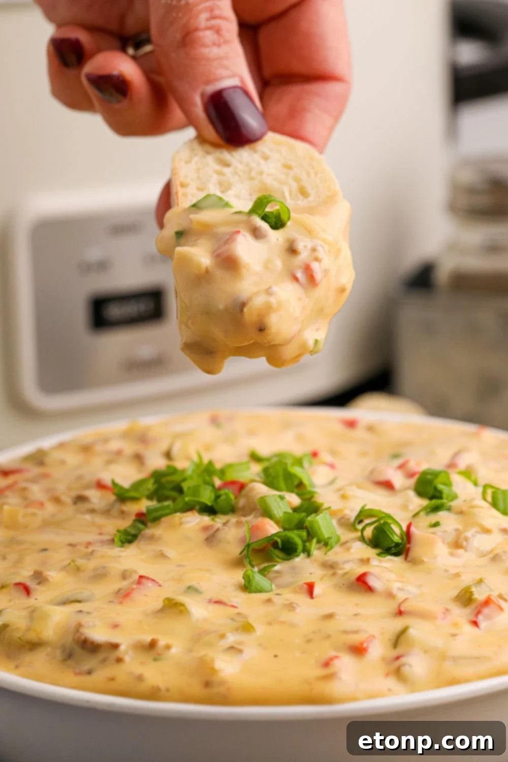 Crock Pot Philly Cheesesteak Dip in a bowl with a sliced bread dipped in the cheese sauce 