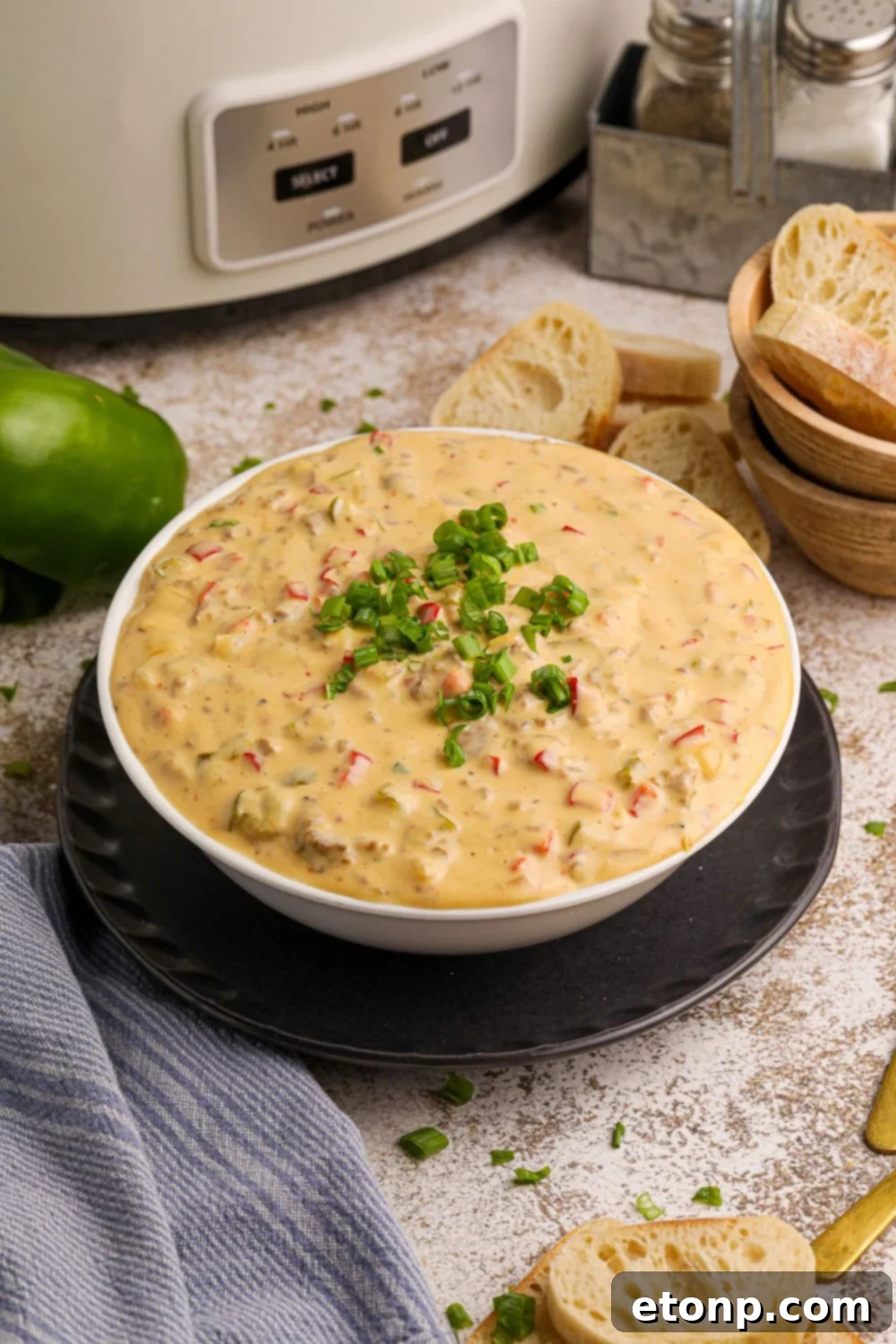 Crock Pot Philly Cheesesteak Dip in a white bowl on table with peppers around it on counter and bread slices