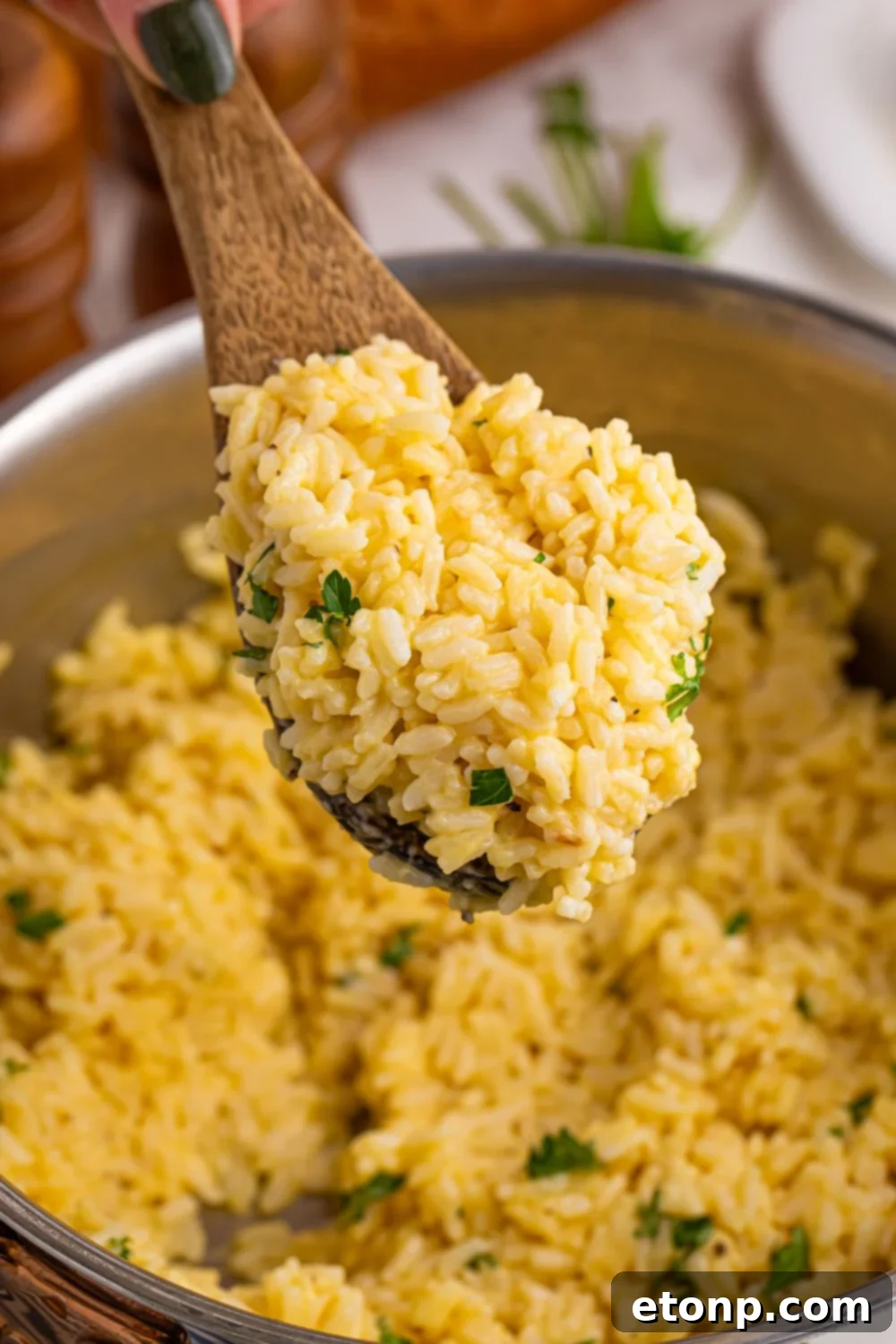 Souper Rice in a pan on table with a wooden spoon with some rice on the spoon being held above the pan