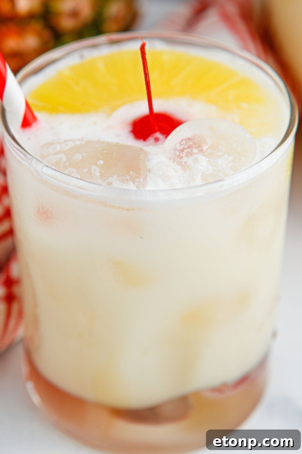 Pina Colada Punch in a glass sitting on a table with a cherry in the center.