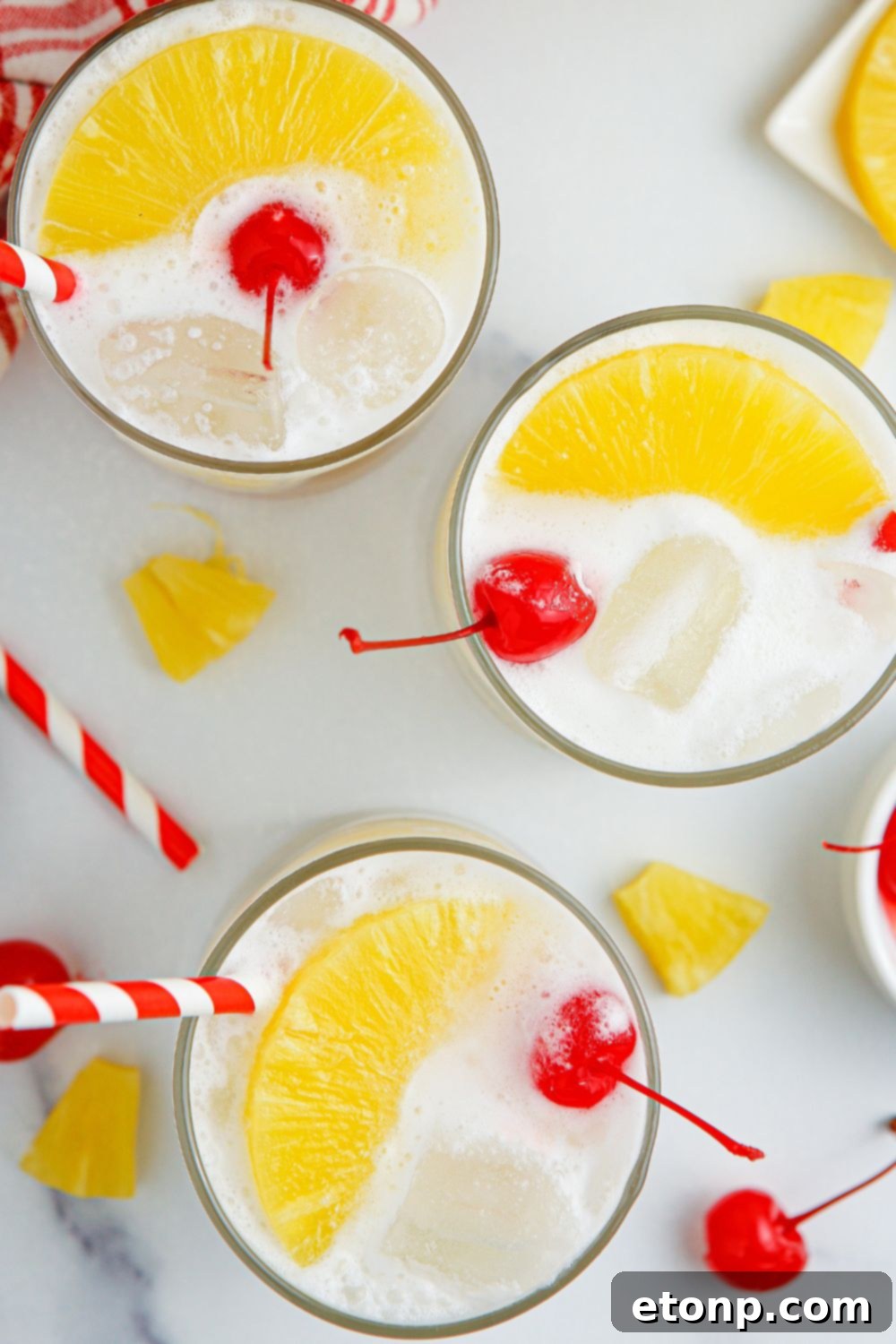 Pina Colada Punch in glasses on a table, each topped with pineapple and a cherry.
