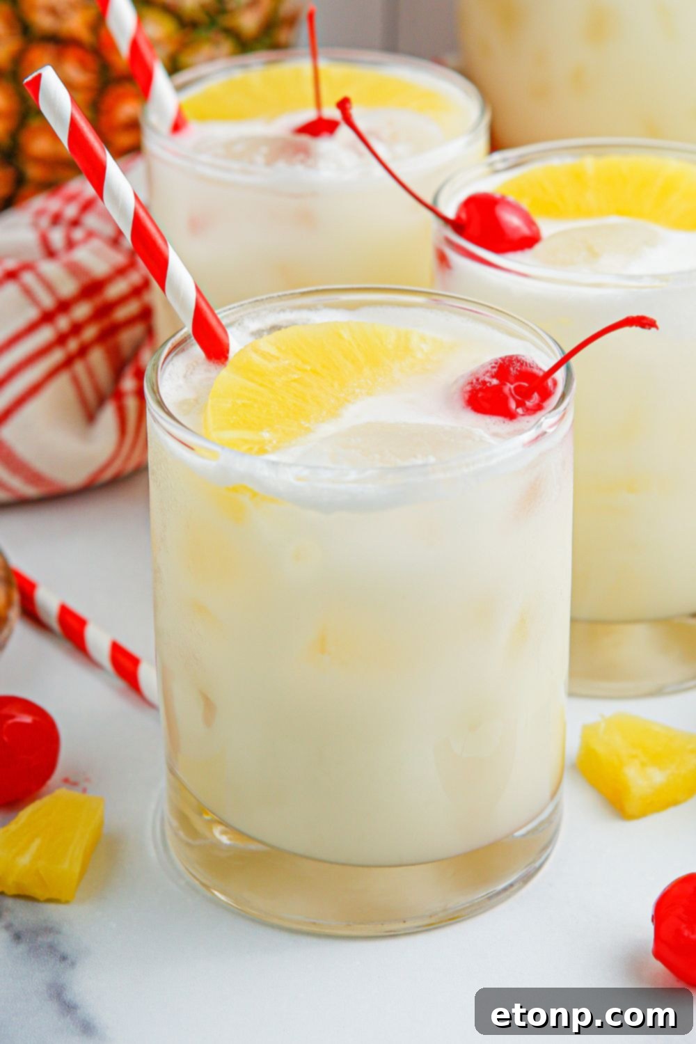 Pina Colada Punch in three glasses sitting on a table with garnishes placed around the glasses.