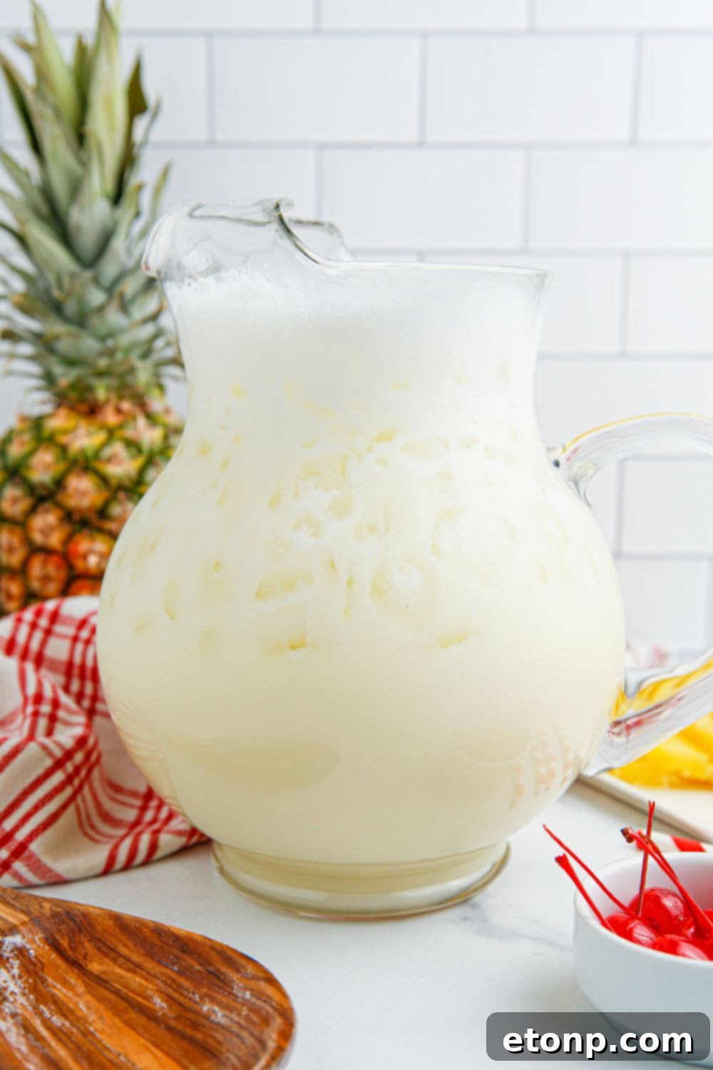 Freshly mixed Pina Colada Punch in a clear glass pitcher, ready to be served.