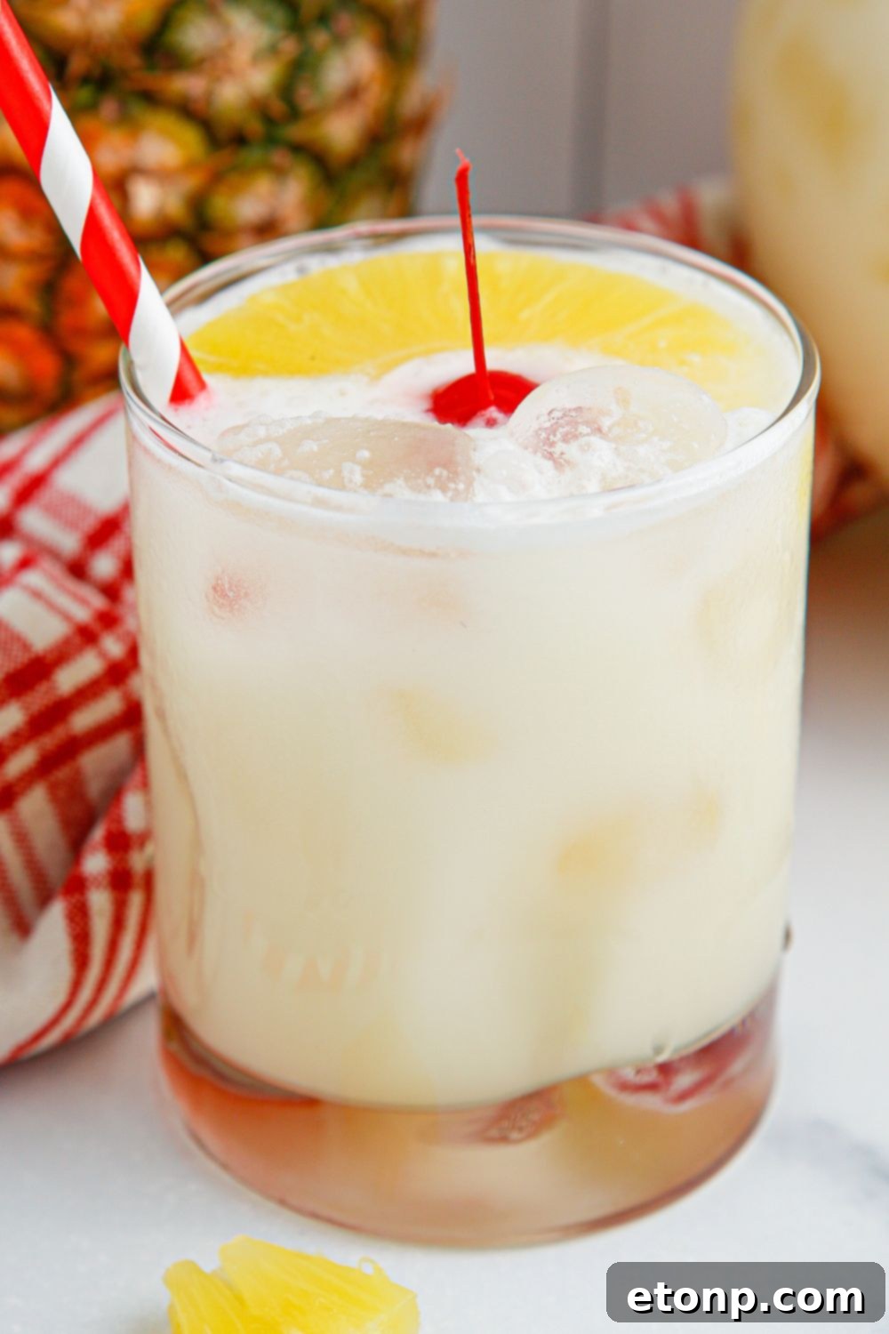 Pina Colada Punch in a small glass with a cherry and pineapple slice garnish, and a red straw.