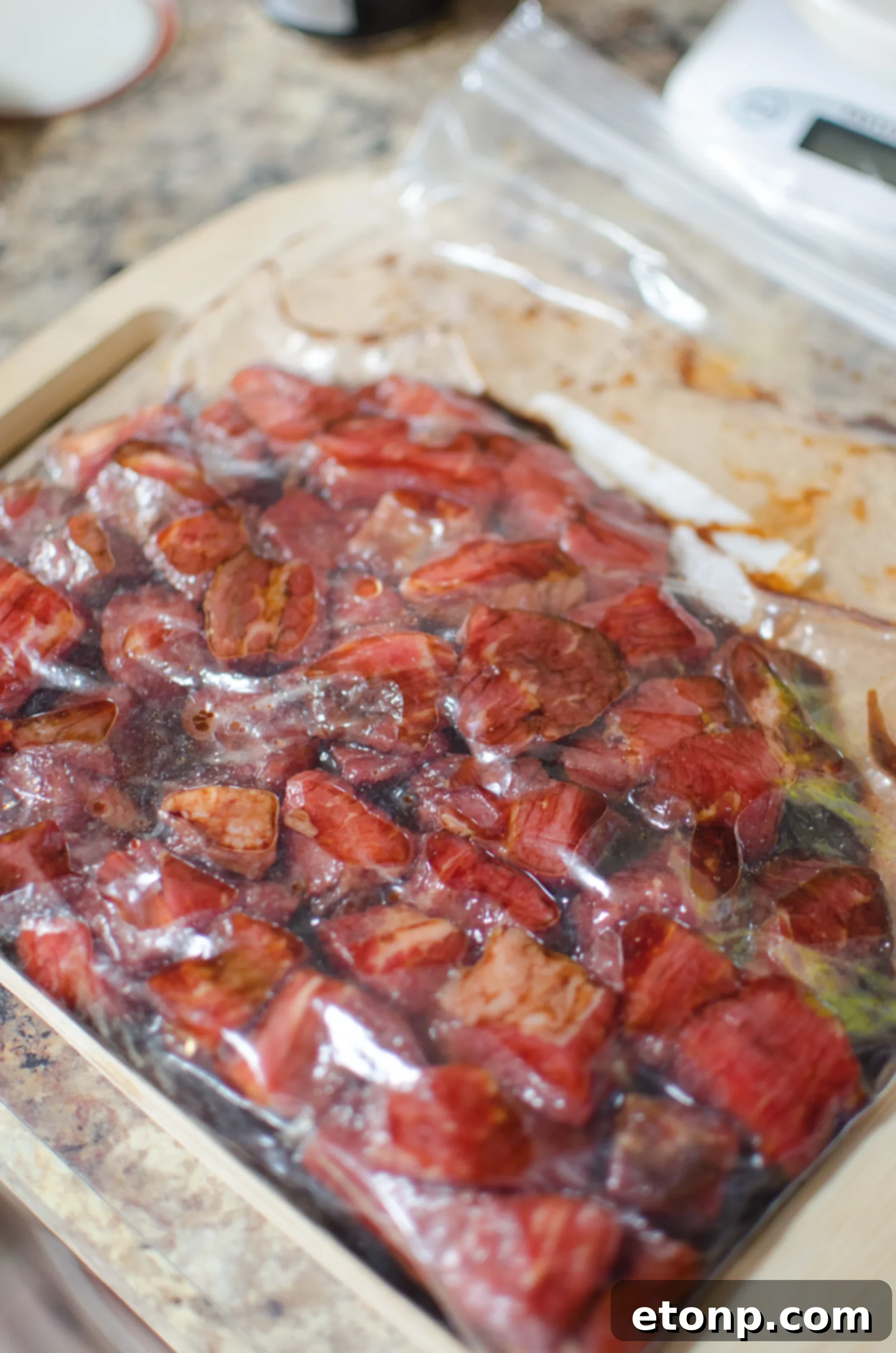 A close-up view of marinated raw sirloin steak pieces with sliced onions and bell peppers.