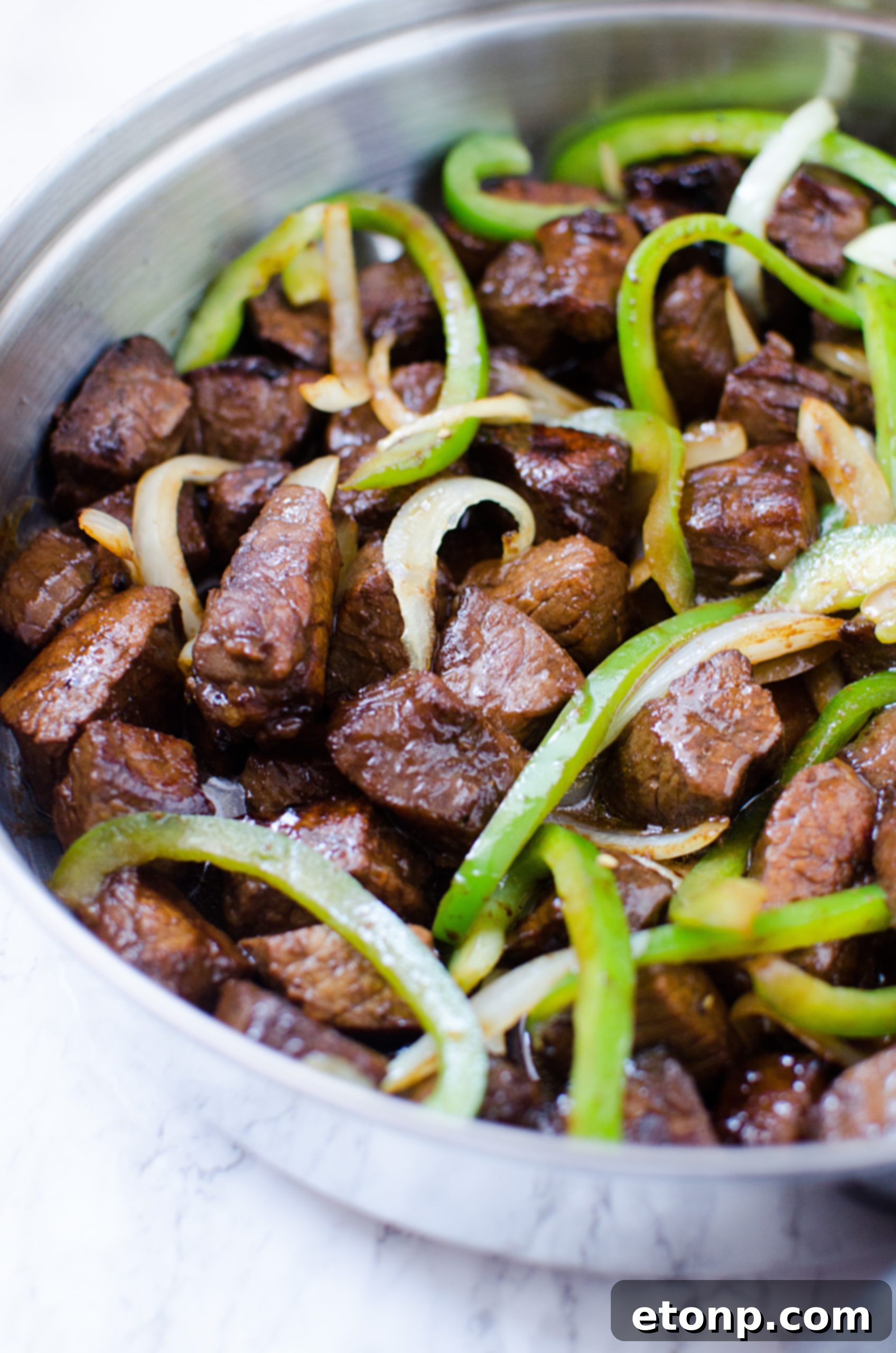 Sirloin steak pieces being tossed in a bowl with the homemade Asian marinade.