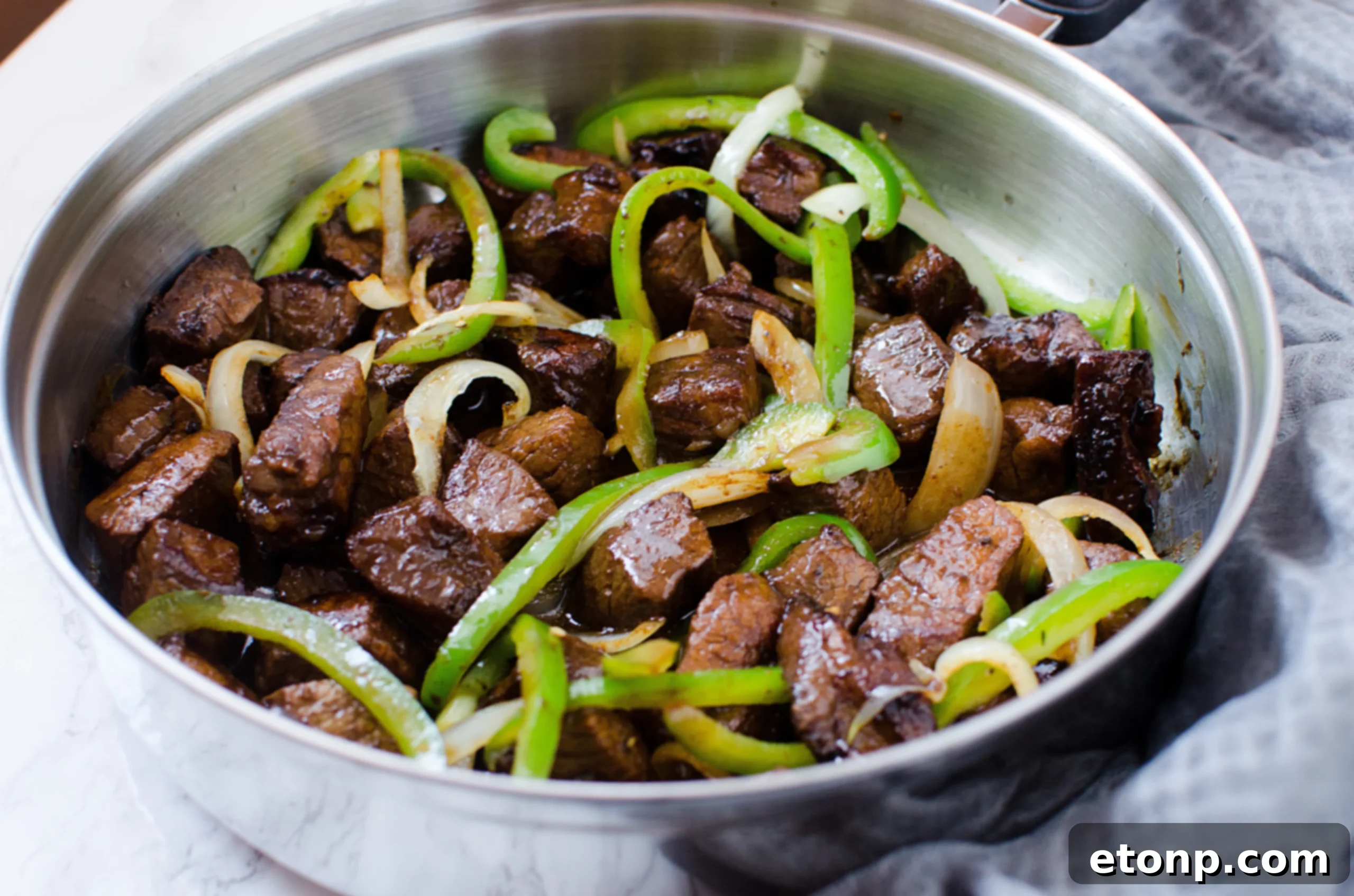 Sautéing sliced onions and bell peppers in a large pan with olive oil.