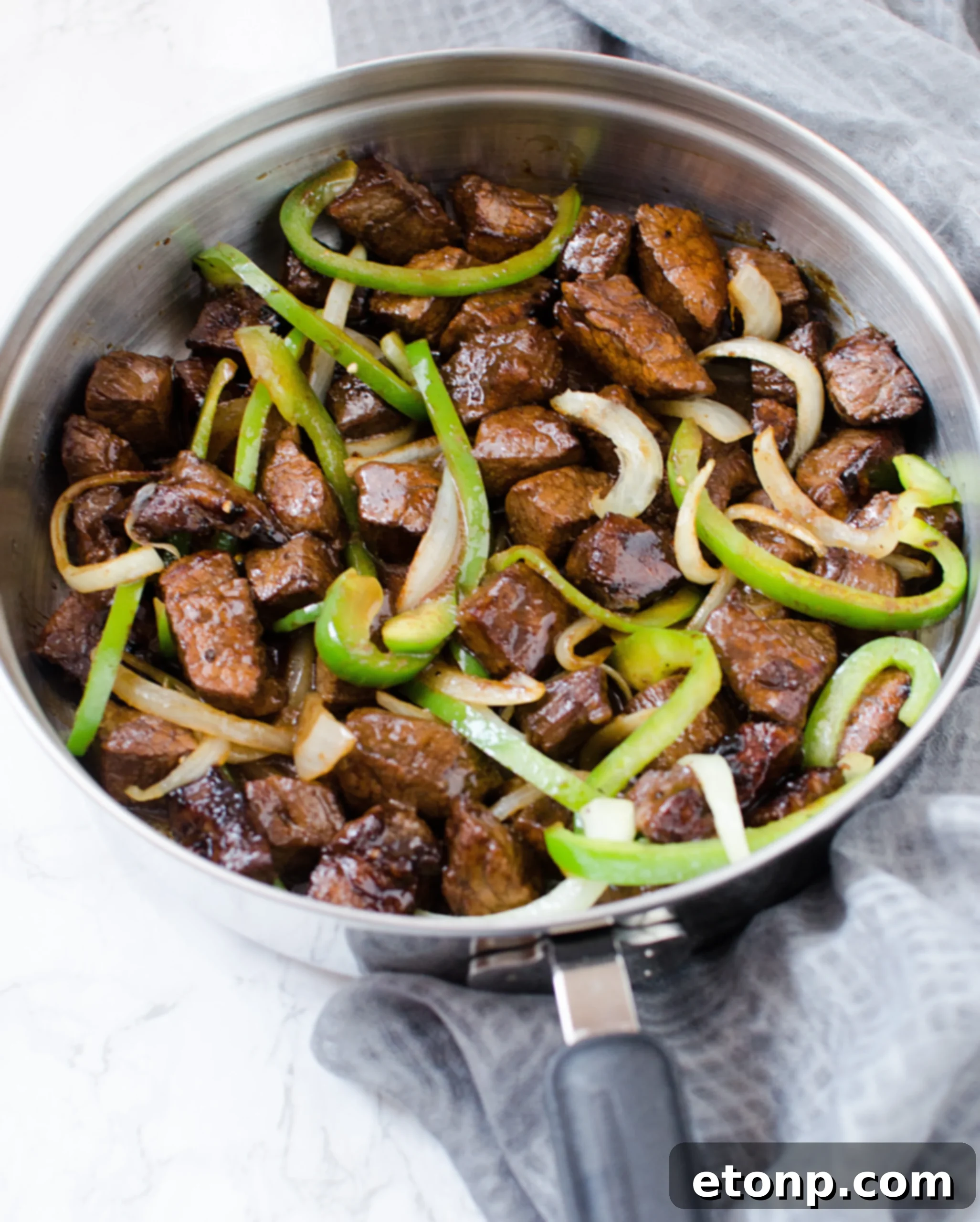 Adding marinated steak pieces to the pan with sautéed vegetables, spreading them into a single layer.
