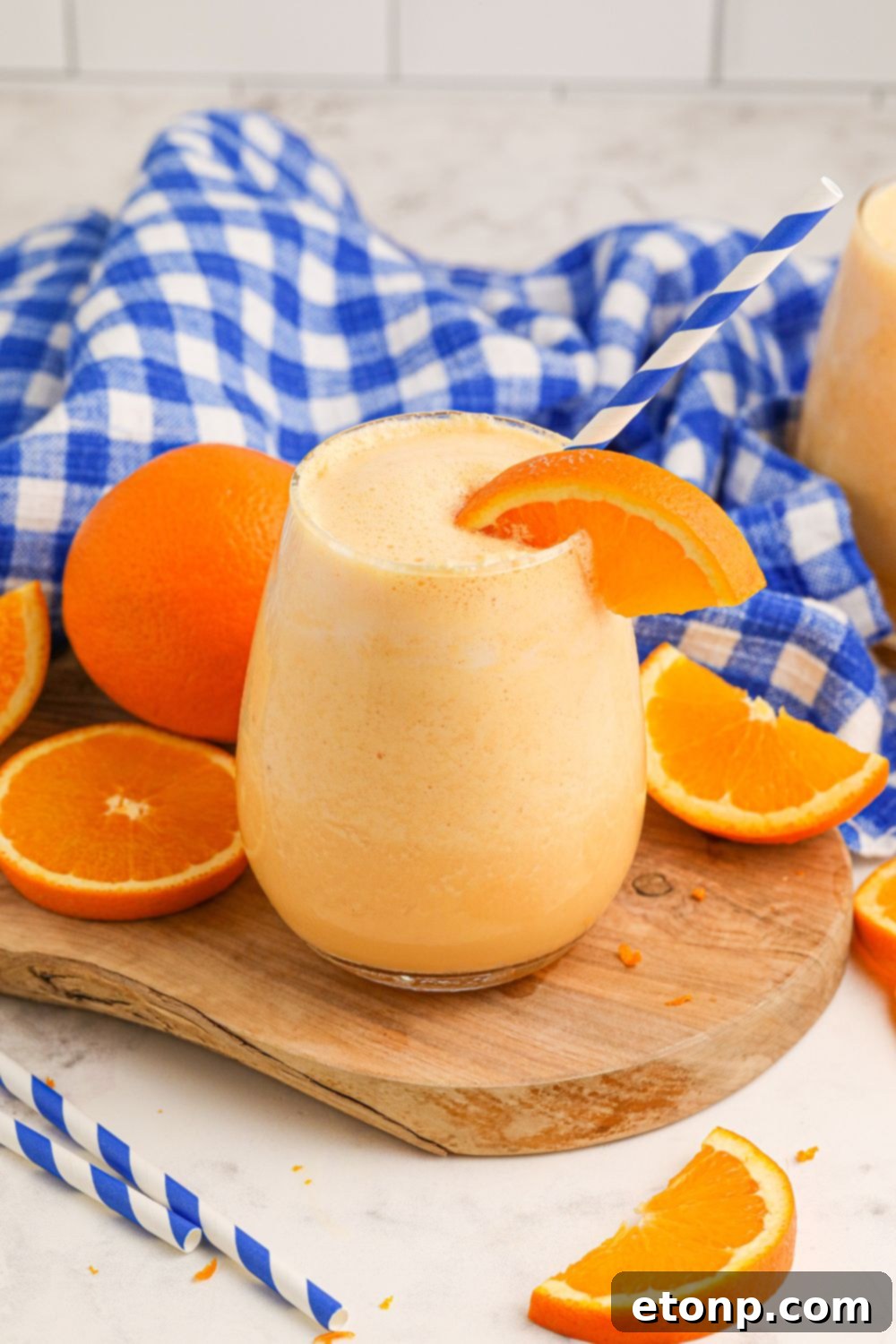 Copycat Orange Julius on table with oranges and slices around it and a blue and white checked towel behind it in background of image 