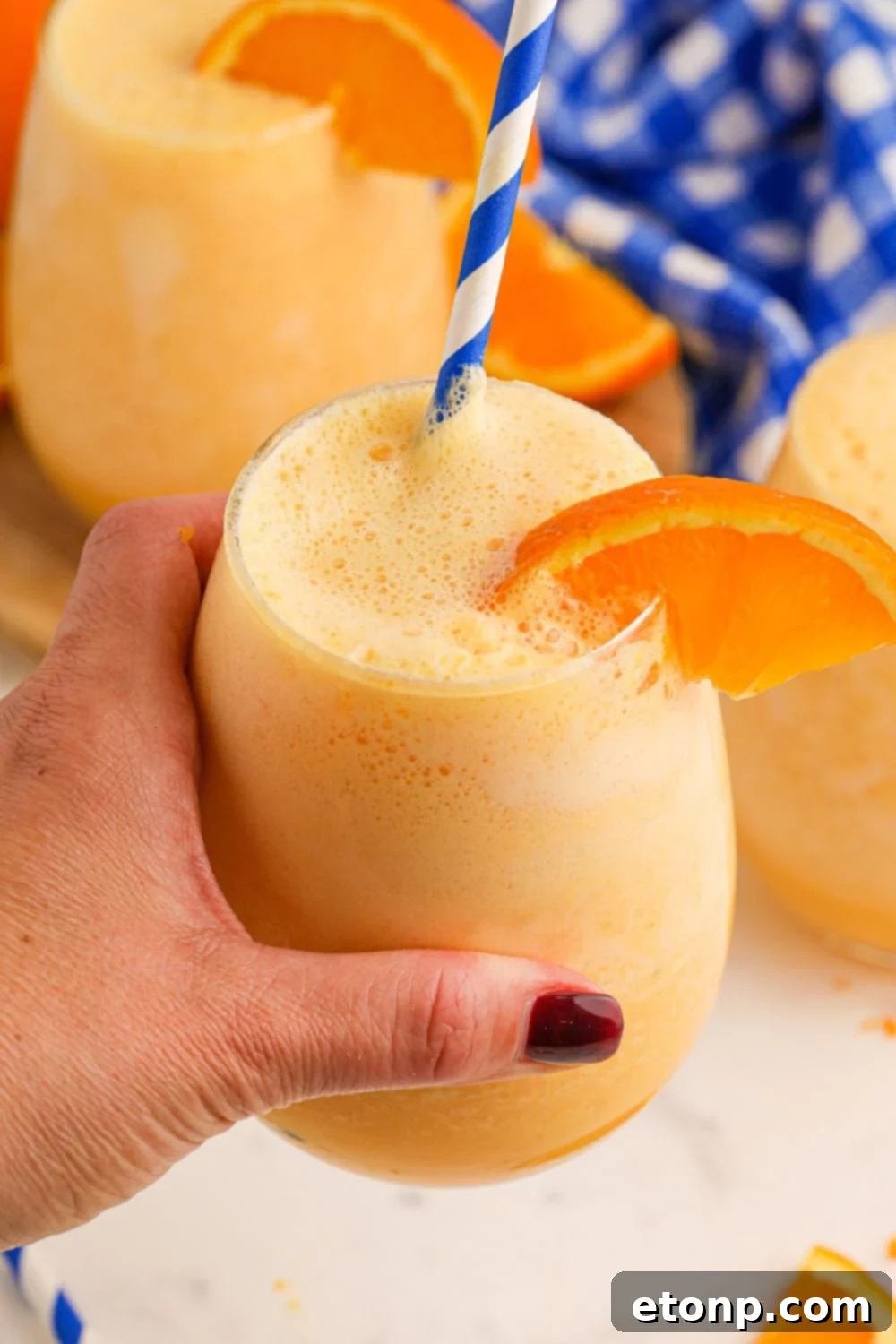 Copycat Orange Julius in a glass in hand with more glasses of julius on table 