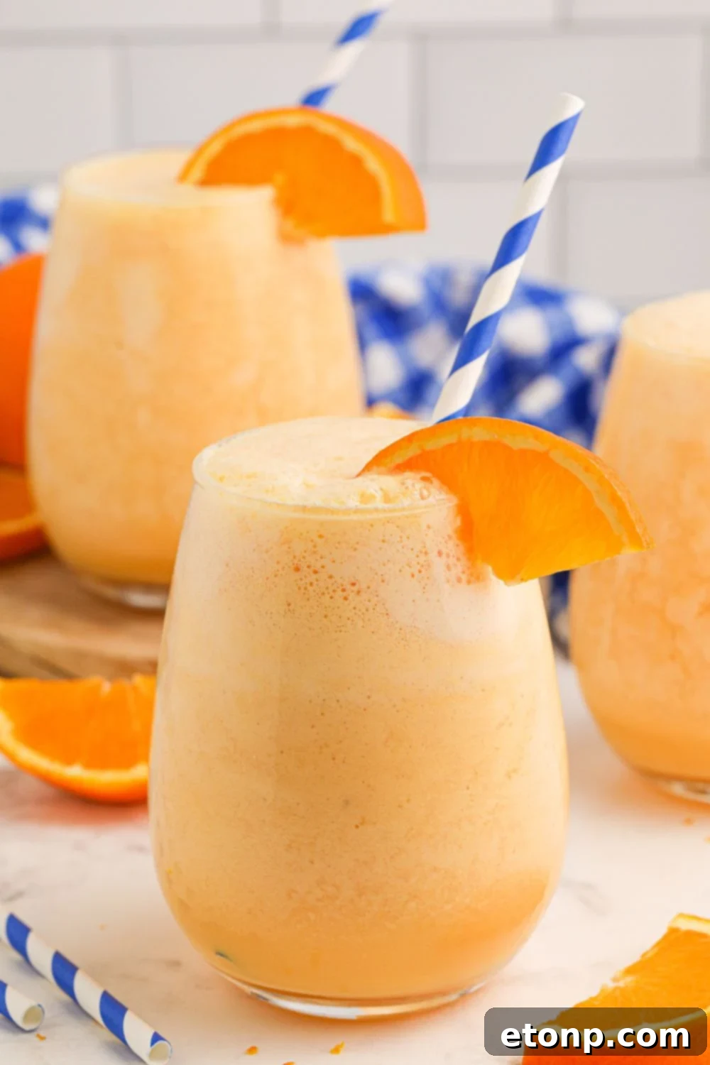 Copycat Orange Julius drinks spread out on table with orange wedge on side of glass and blue and white striped straws 
