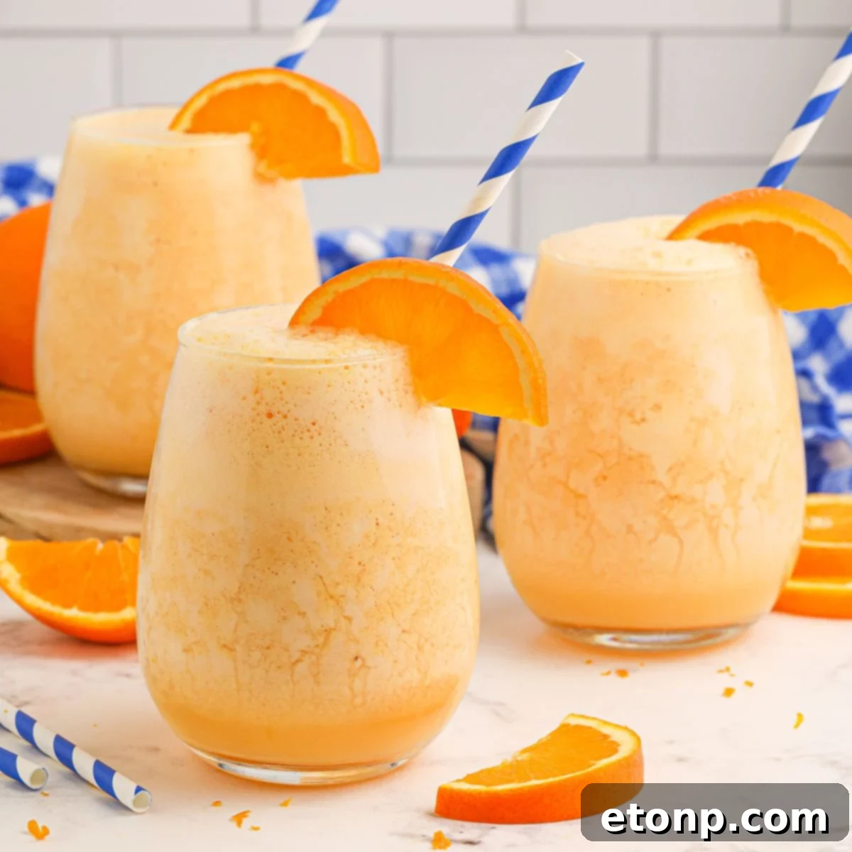 Copycat Orange Julius in three glasses on table with an orange slice on rim and straw in each glass 