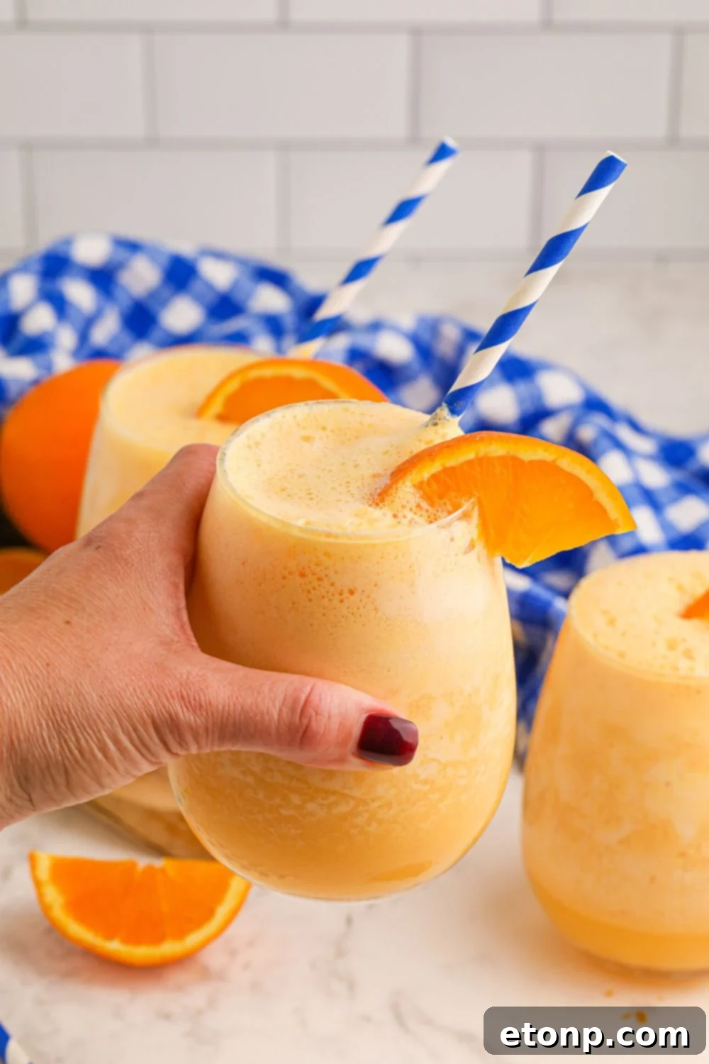 Copycat Orange Julius in hand and two more glasses of Julius on table with orange wedges around it 