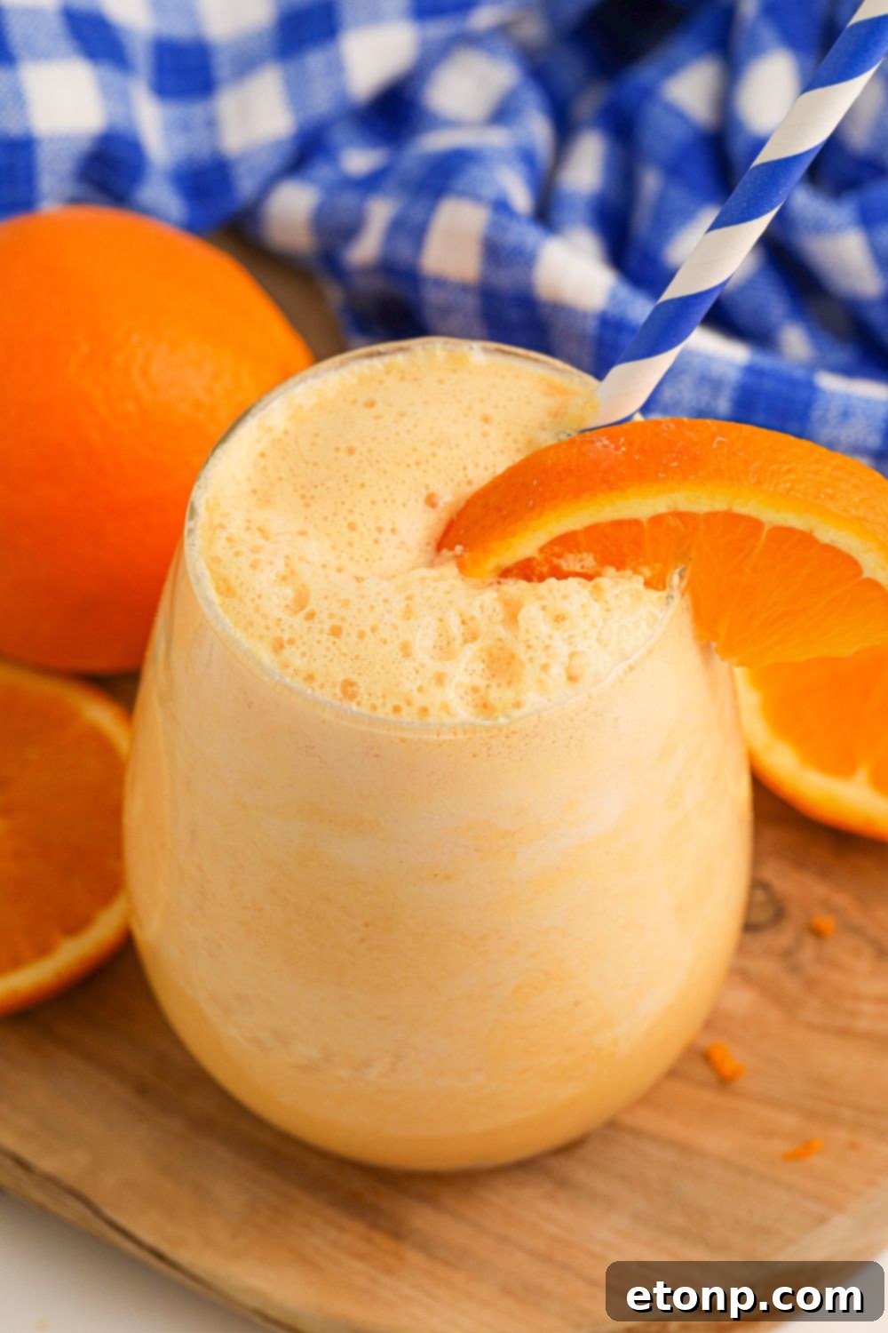 Copycat Orange Julius on a wooden cutting board and an orange slice on side of cup 