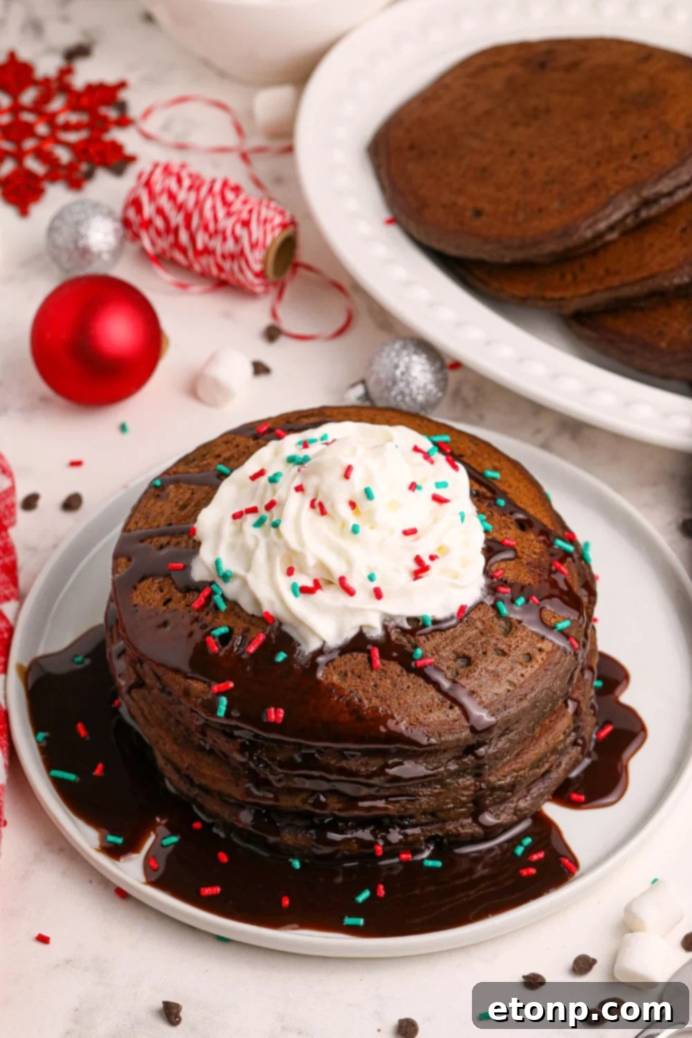 A delightful plate of Hot Chocolate Pancakes topped with whipped cream and festive Christmas decor in the background, creating a cozy holiday atmosphere.