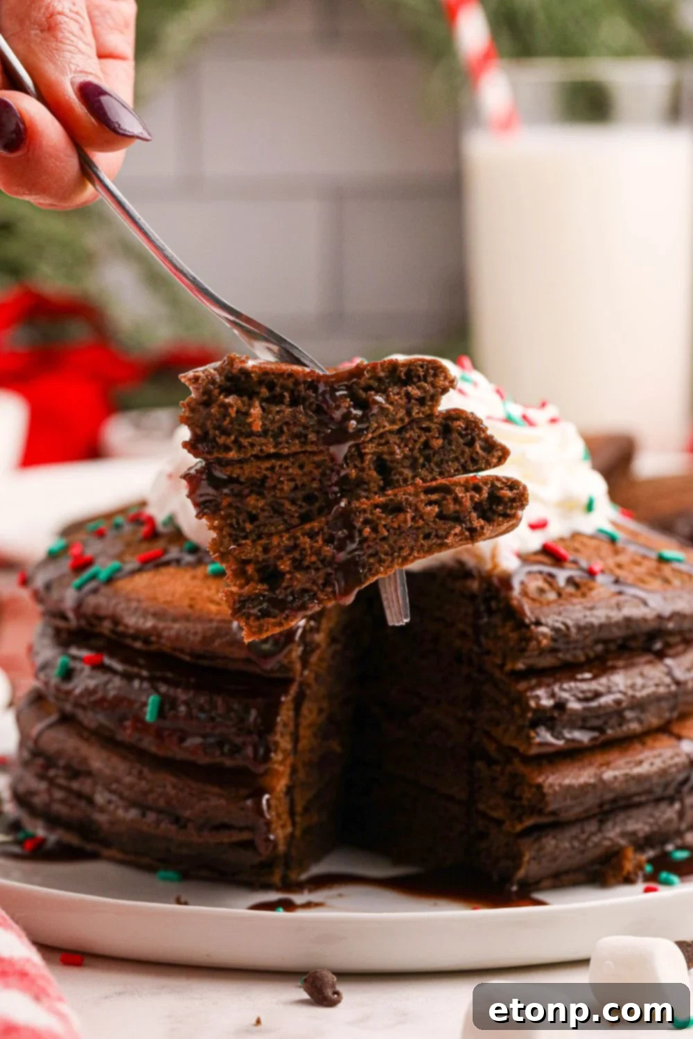 A fork holding a piece of fluffy Hot Chocolate Pancake, with a plate of stacked pancakes subtly blurred in the background, inviting a delicious bite.