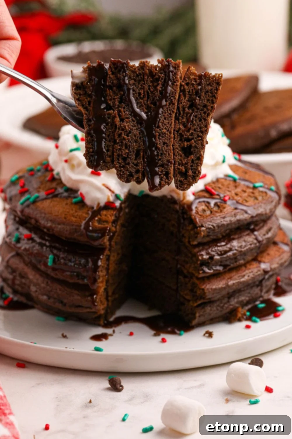 A fork holding a bite-sized piece of Hot Chocolate Pancake, with a plate of more delicious pancakes visible in the background on the table.