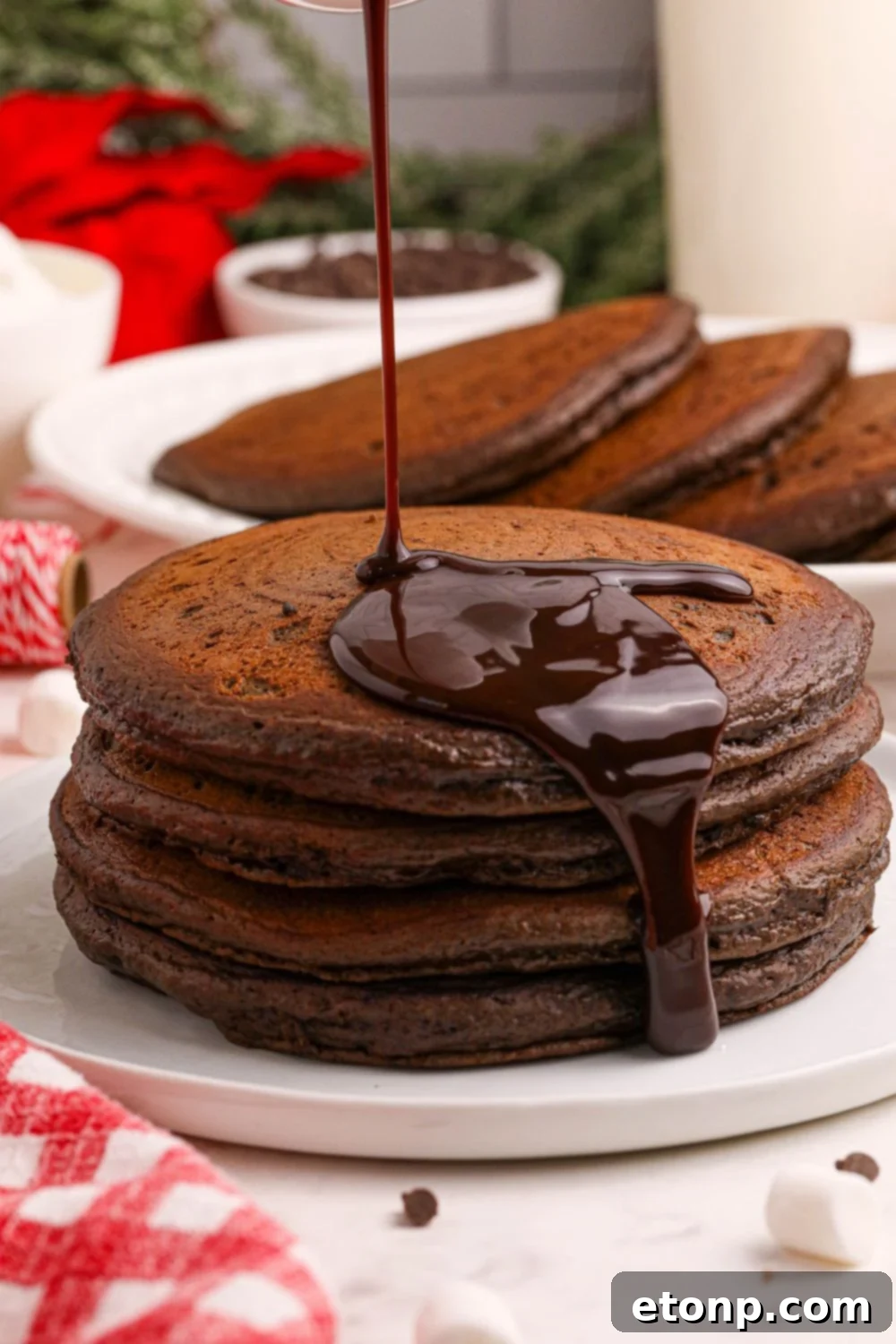 Delicious Hot Chocolate Pancakes expertly stacked on a white plate, with a stream of rich chocolate syrup cascading over the sides, creating an irresistible visual treat.