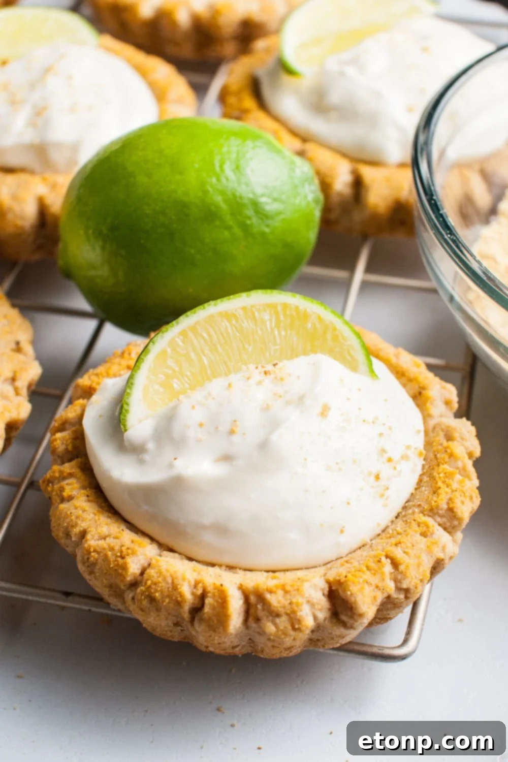 Crumbl Key Lime Pie Cookies on a wire cooling rack with a lime wedge on each cookies and then a full lime on table