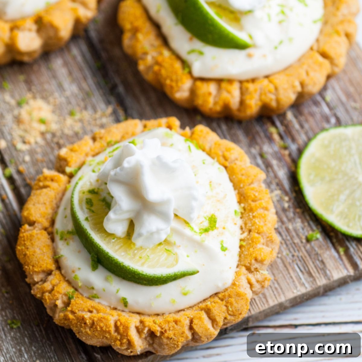 Crumbl Key Lime Pie Cookies on table with lime wedges around and piles of graham cracker crumbs