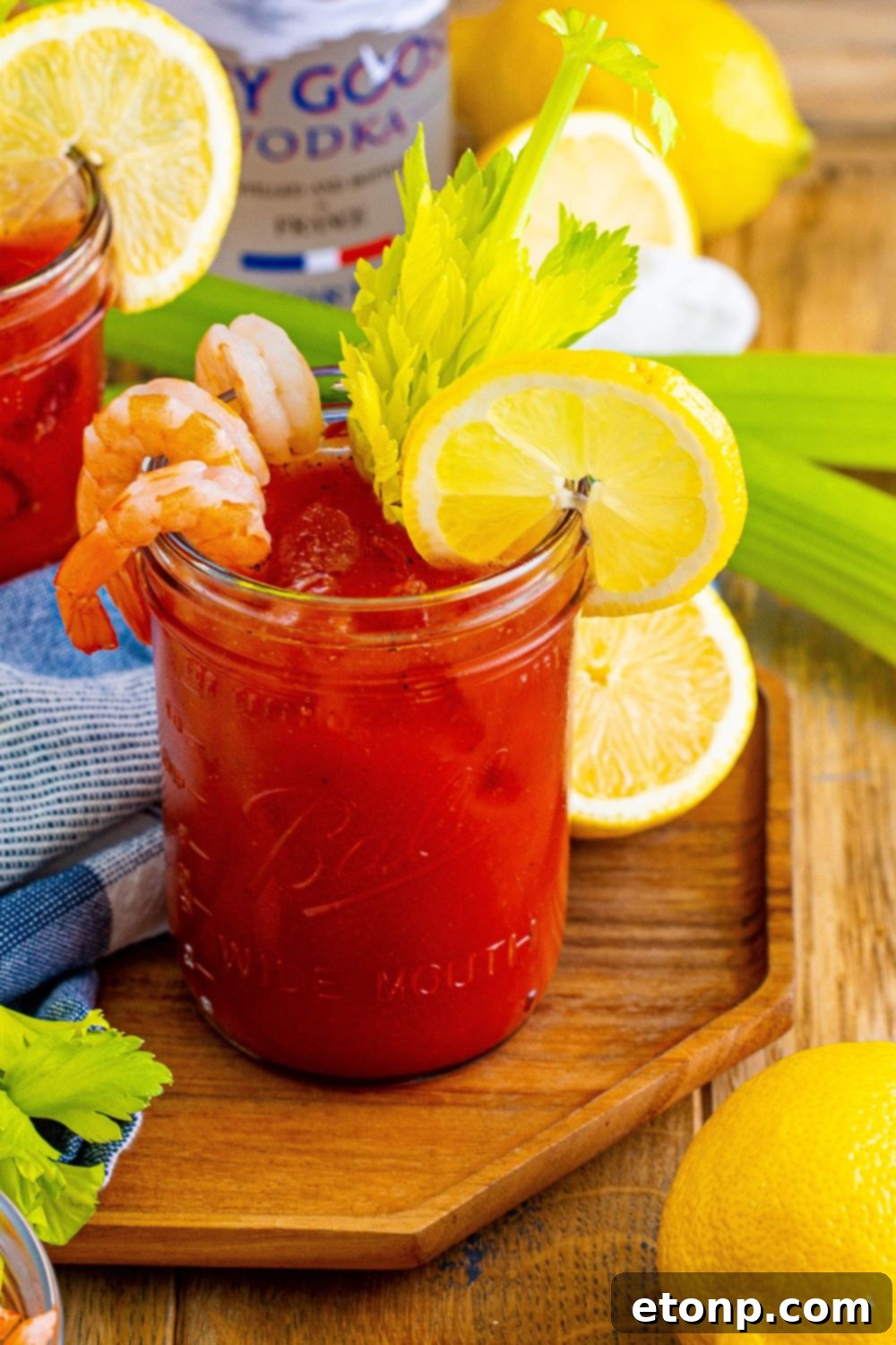 Freshly prepared Bloody Mary cocktails on a rustic cutting board, surrounded by vibrant celery stalks and bright lemon slices, highlighting fresh garnishes.