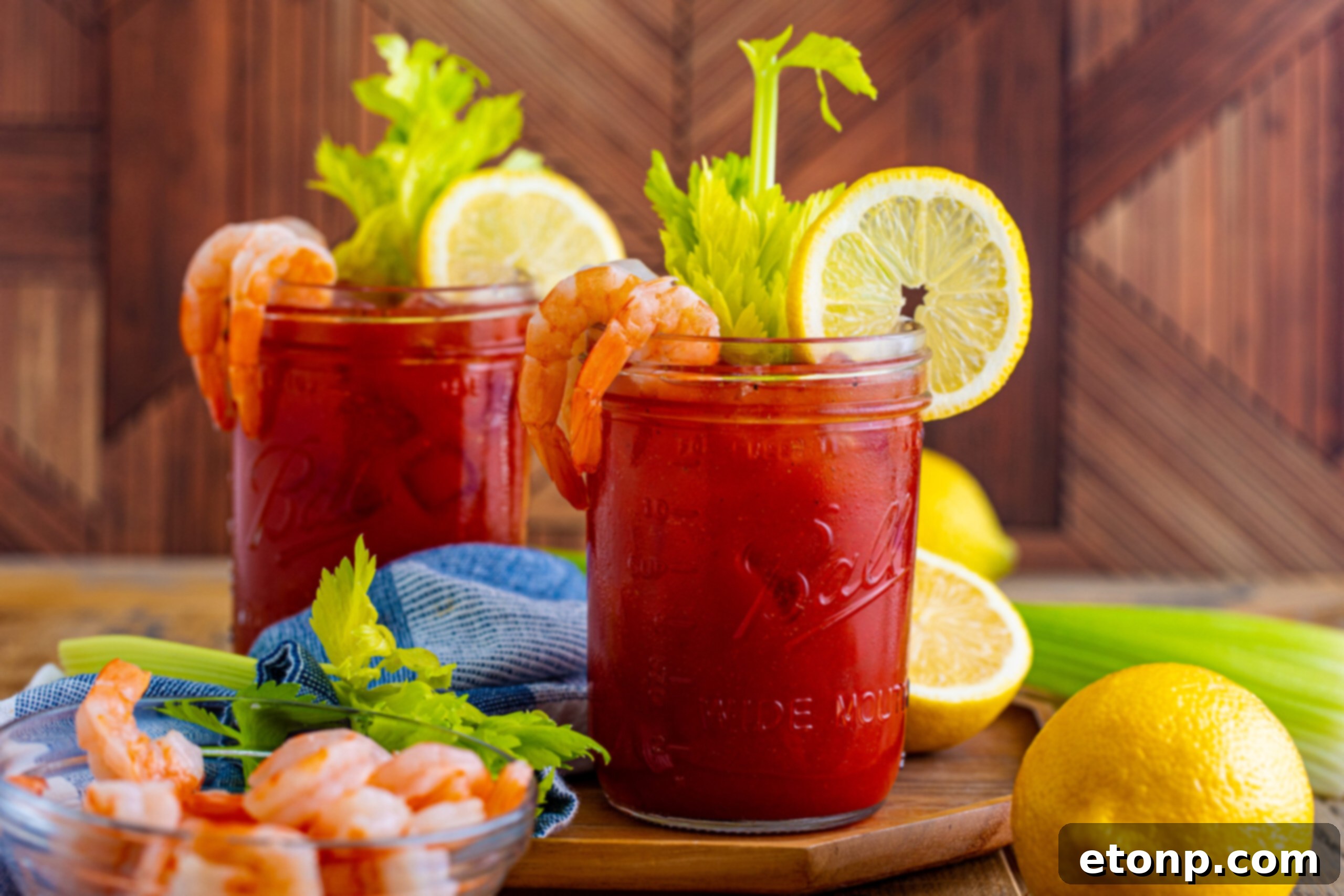 A vibrant Bloody Mary in a clear mason jar glass, exquisitely garnished with a tall celery stalk, a bright lemon slice, and a perfectly cooked shrimp, set on a wooden table.