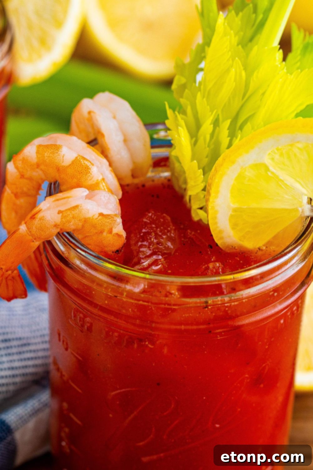 Close-up of a Bloody Mary cocktail, featuring a large shrimp delicately balanced on the rim of the glass, a vibrant lemon wedge, and a crisp celery stick, showcasing elegant garnishing.
