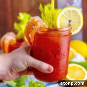 A hand holding a garnished Bloody Mary cocktail above a table, ready to be enjoyed.