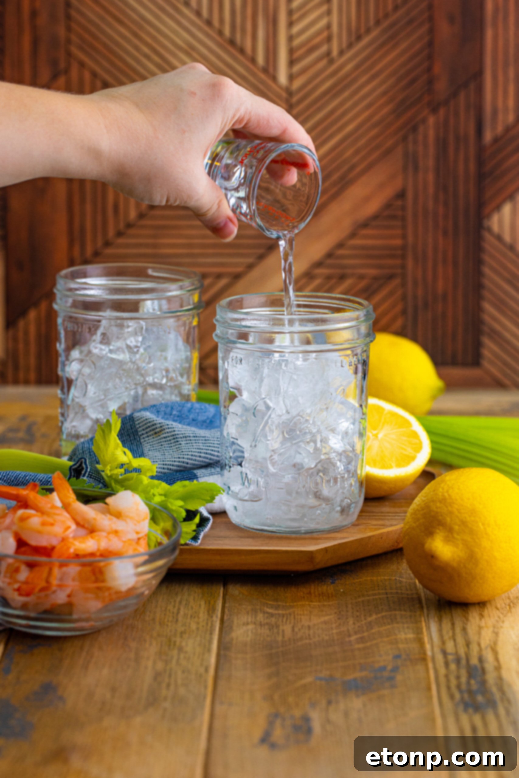Pouring vodka over ice into a clear glass, a crucial first step in preparing a Bloody Mary cocktail.
